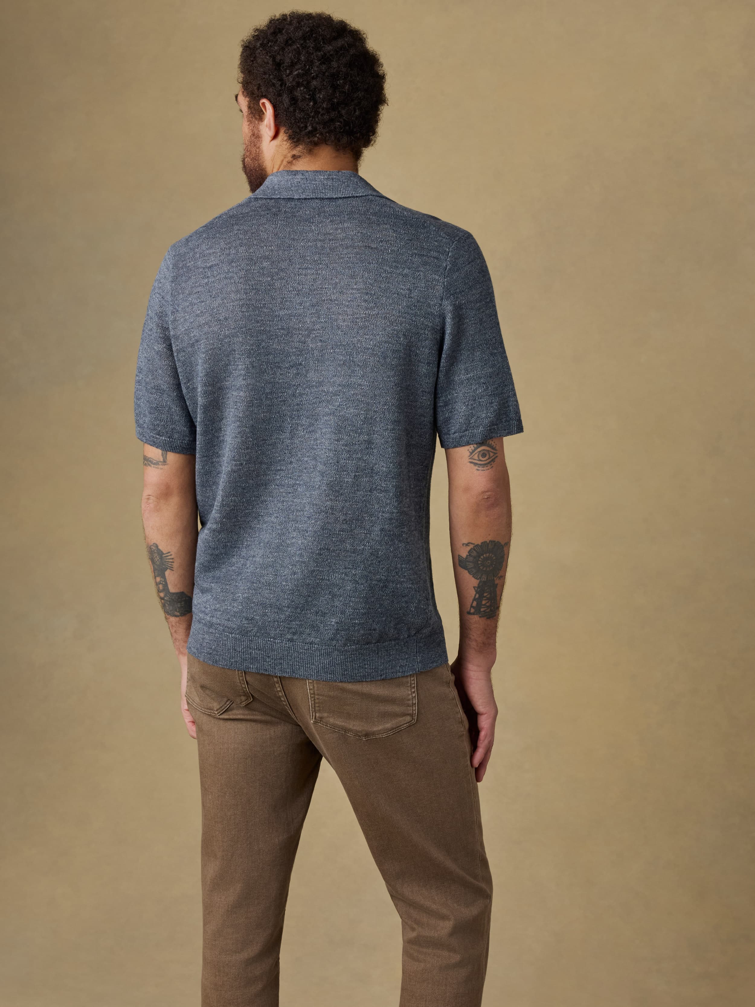 Man wearing a blue polo shirt and brown pants against a beige background