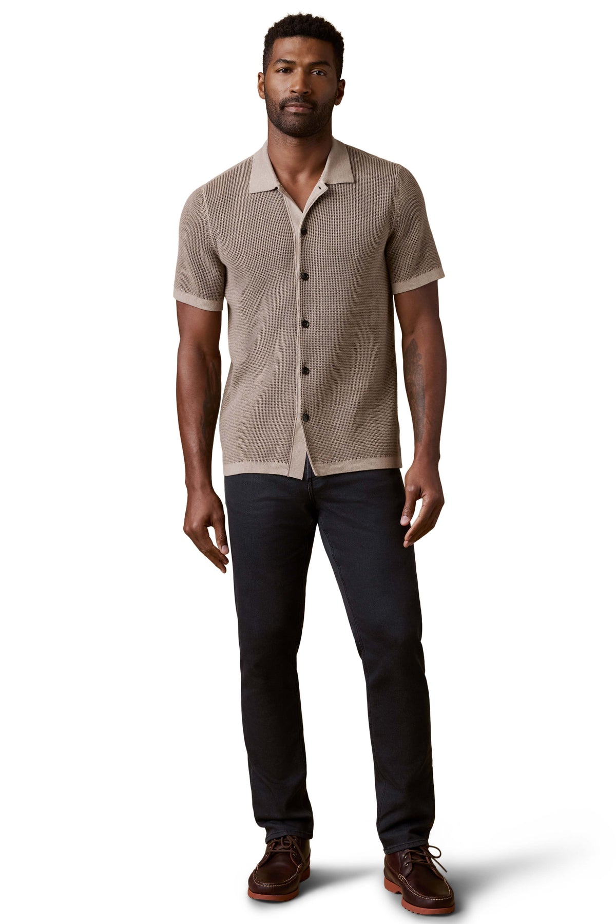 A man wearing a brown polo, dark jeans, and brown shoes, image 2 of 3