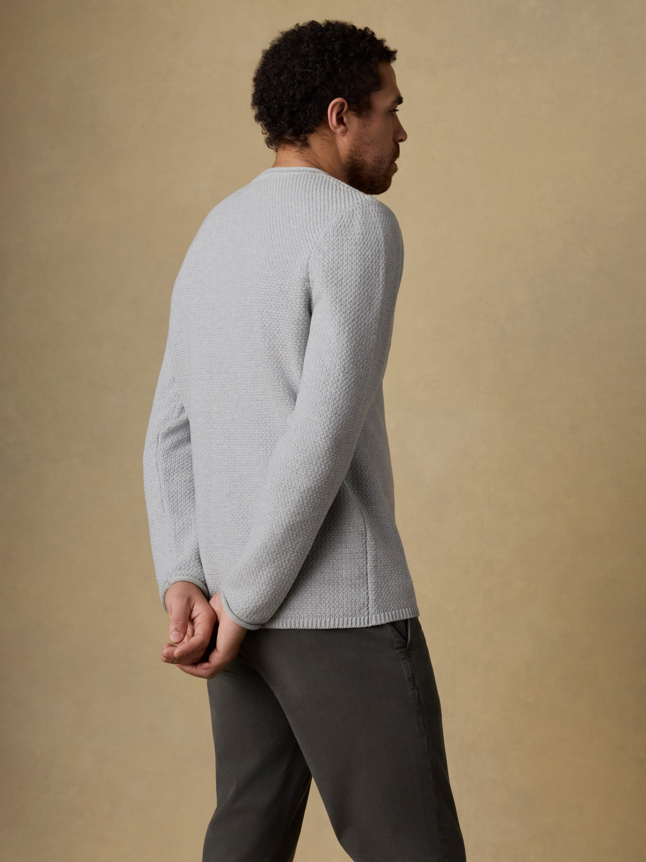 Back view of a man wearing a gray sweater and black jeans against a beige background
