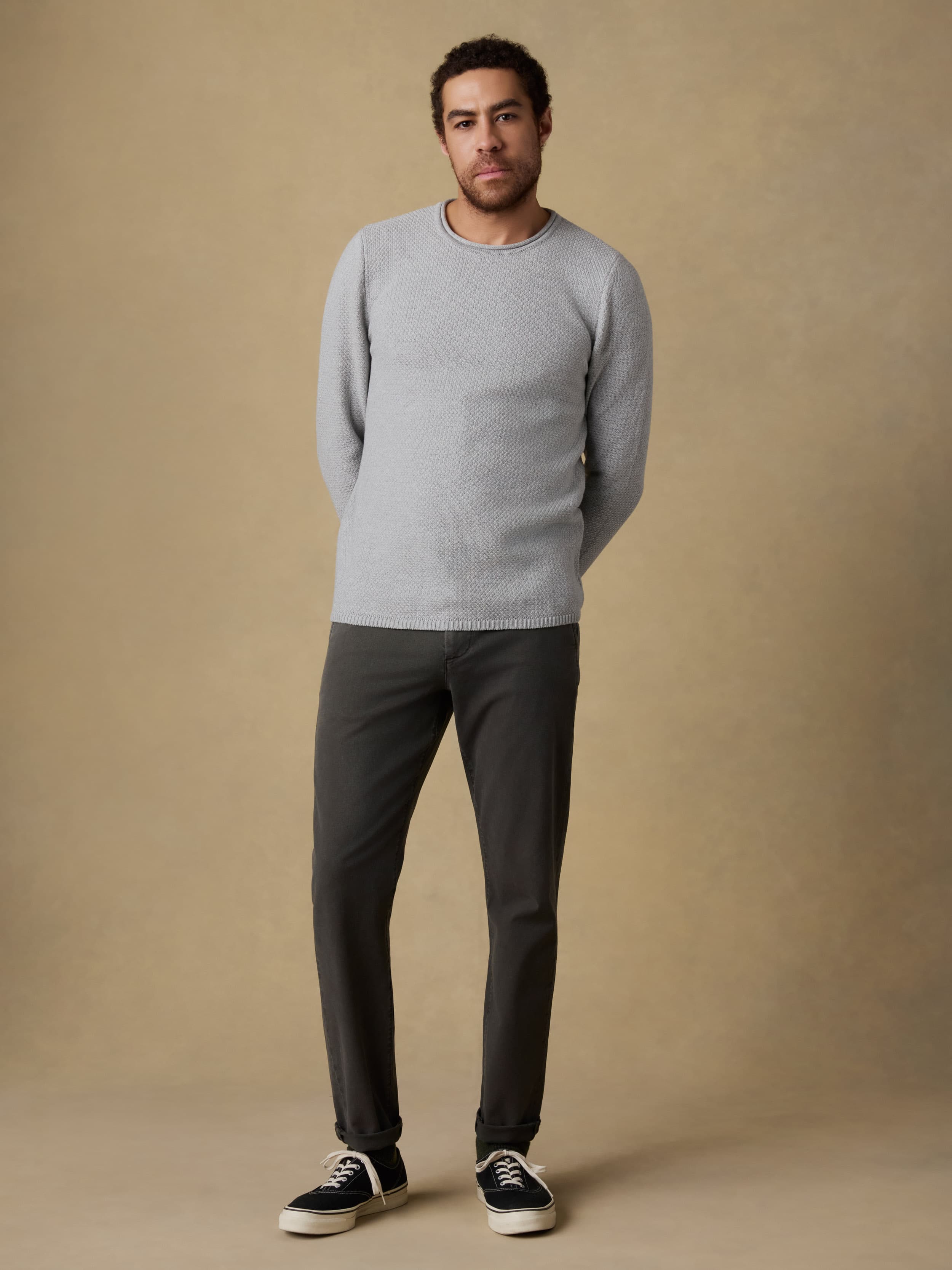 Man wearing a gray sweater and black jeans against a beige background