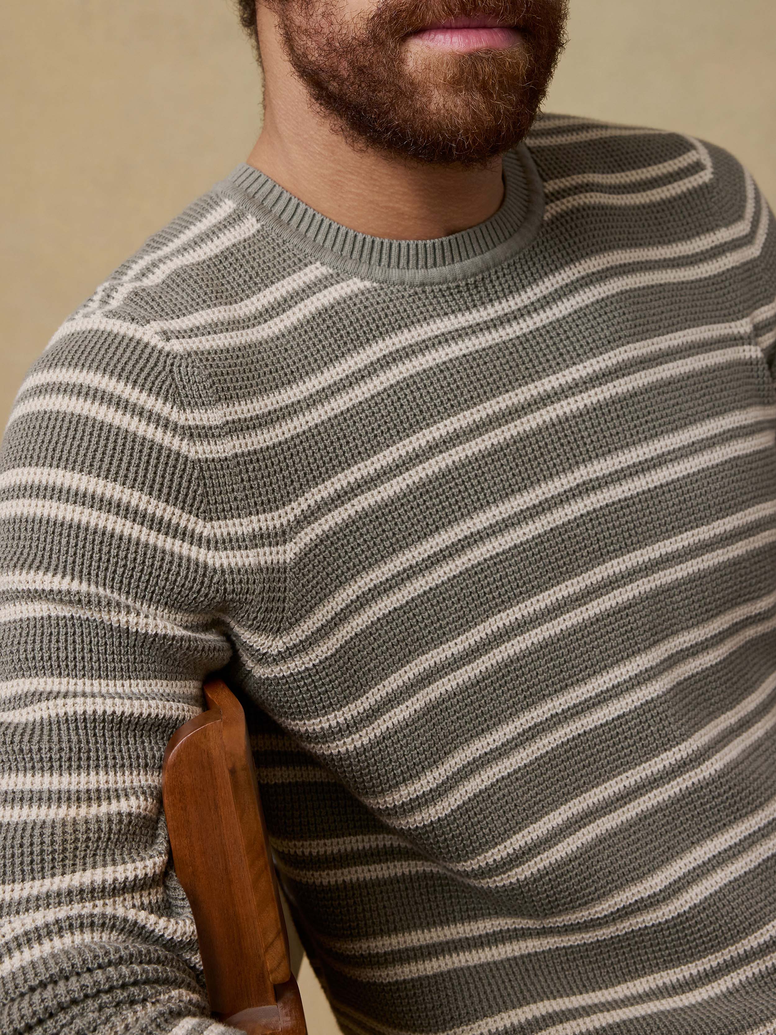 Detail shot of a man sitting on a chair  wearing a green striped sweater against a beige background
