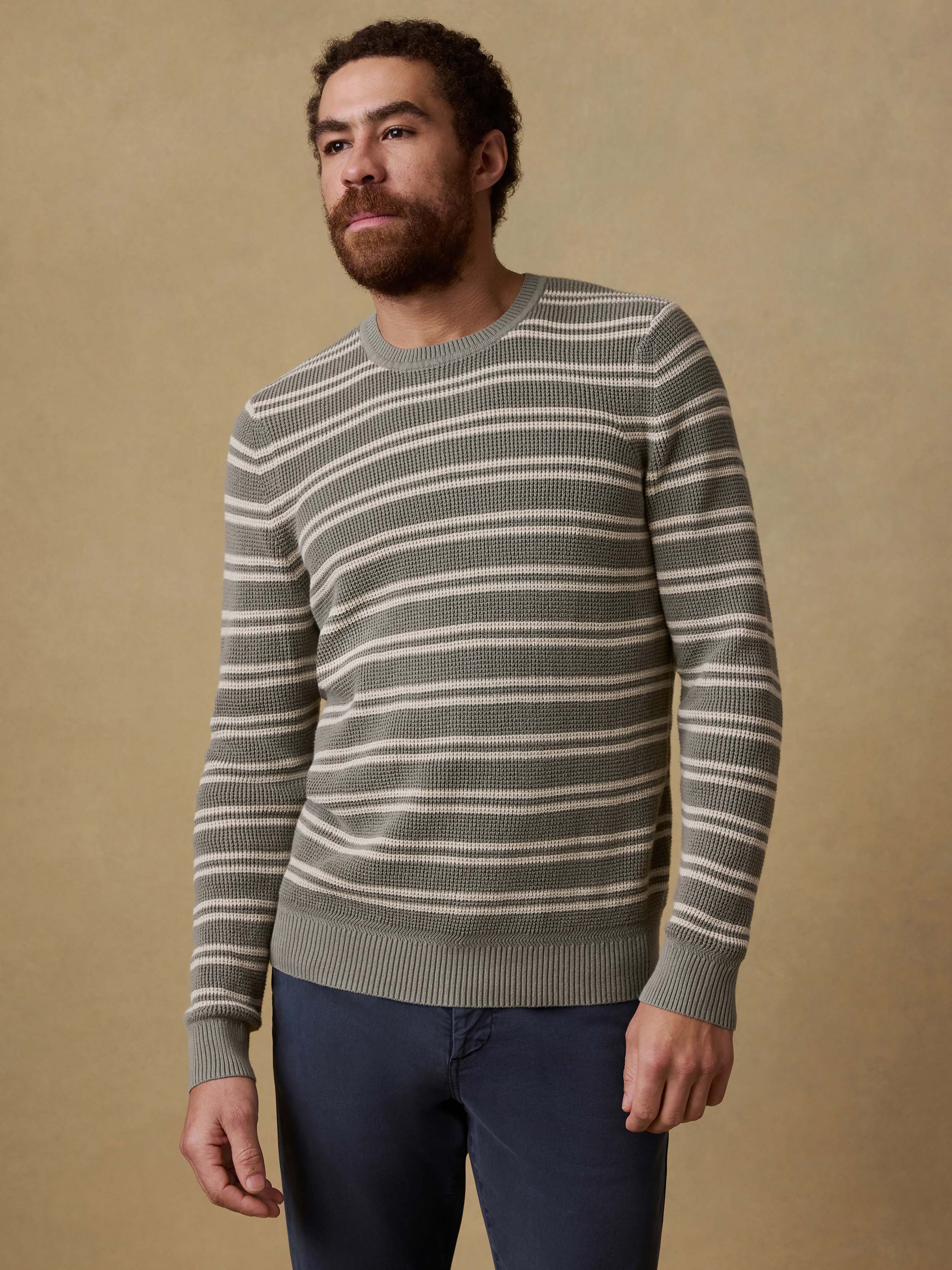Man wearing a green striped sweater and navy pants against a beige background