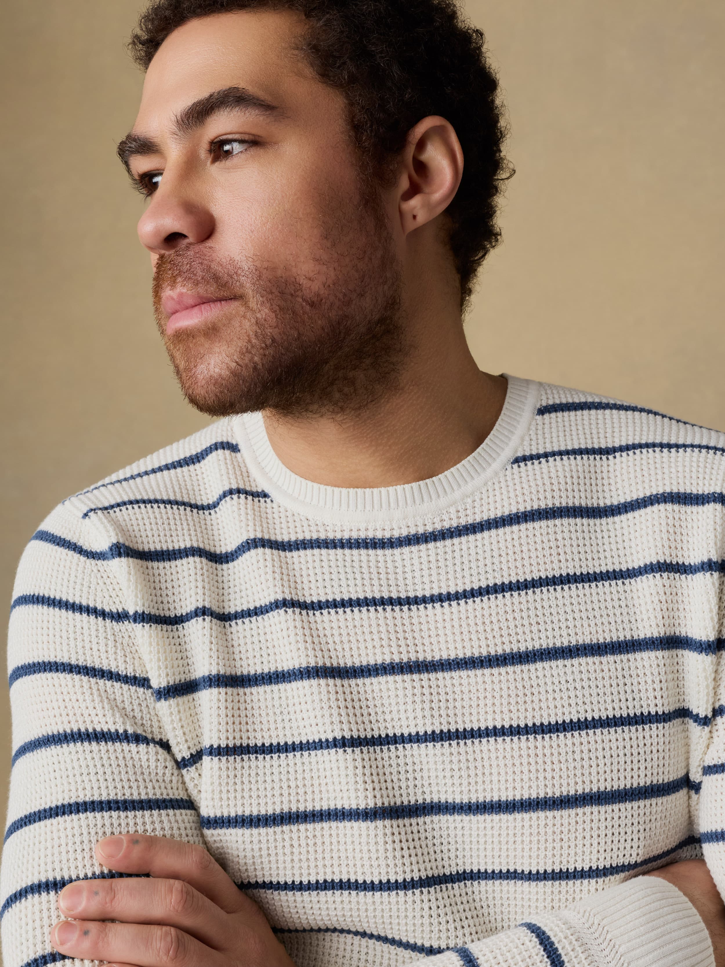 Man wearing a white and blue striped crewneck sweater against a beige background