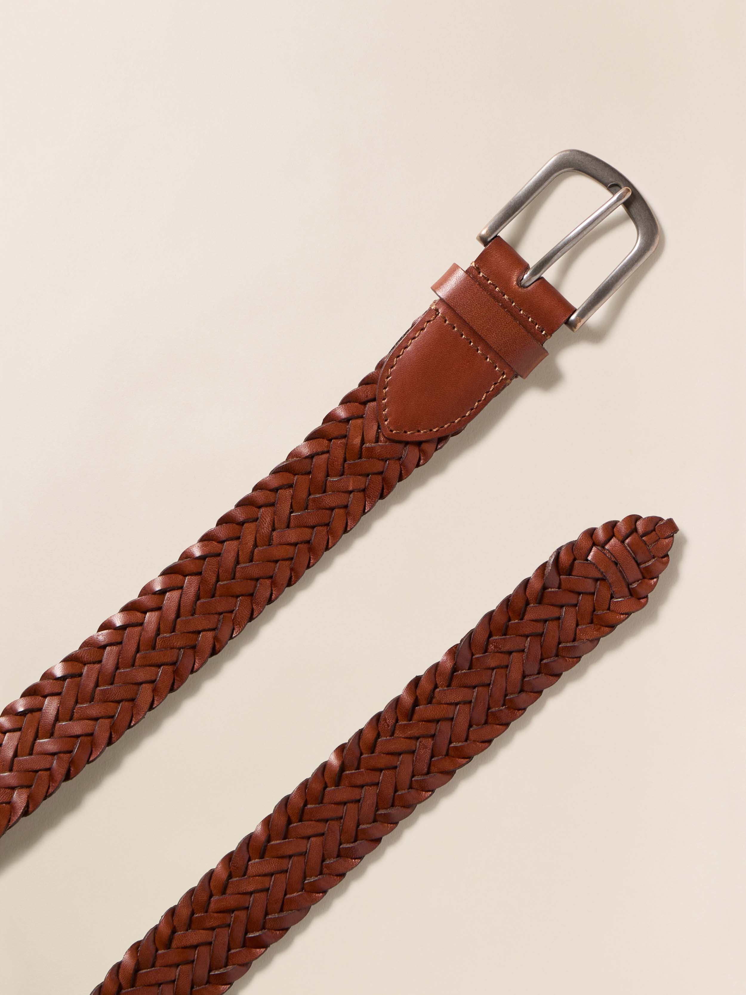 Brown braided leather belt with a silver buckle on a beige background