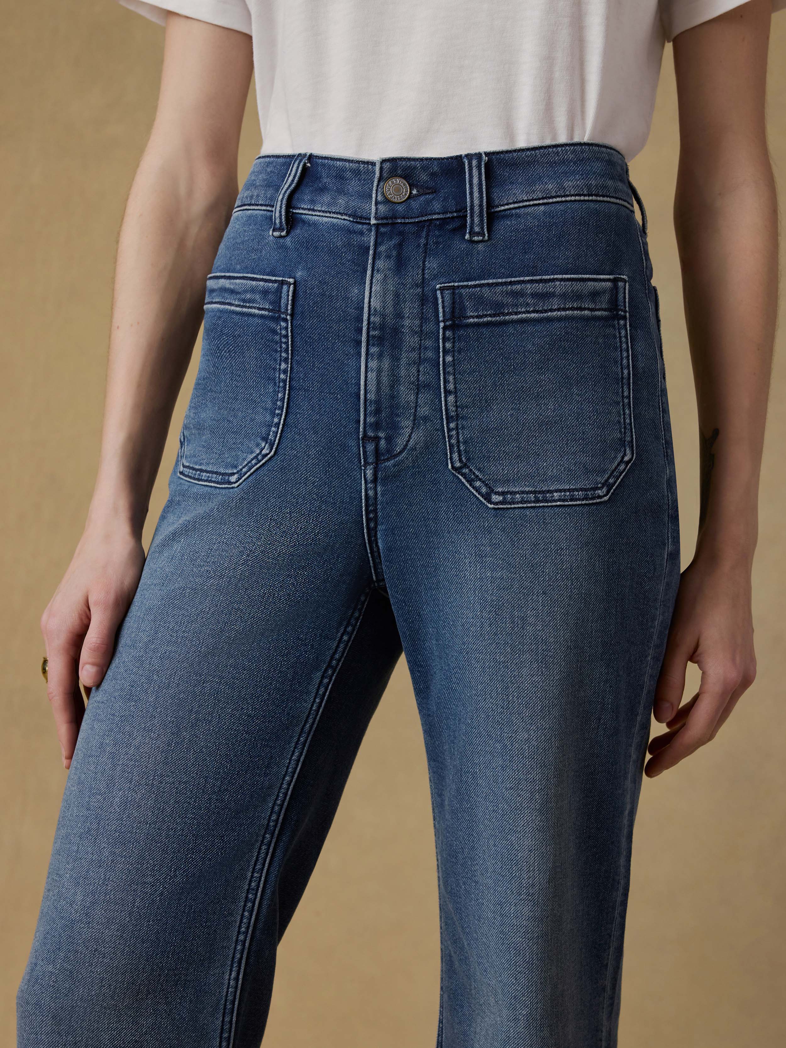 Detail shot of a woman wearing a white t-shirt and blue jeans against a beige background
