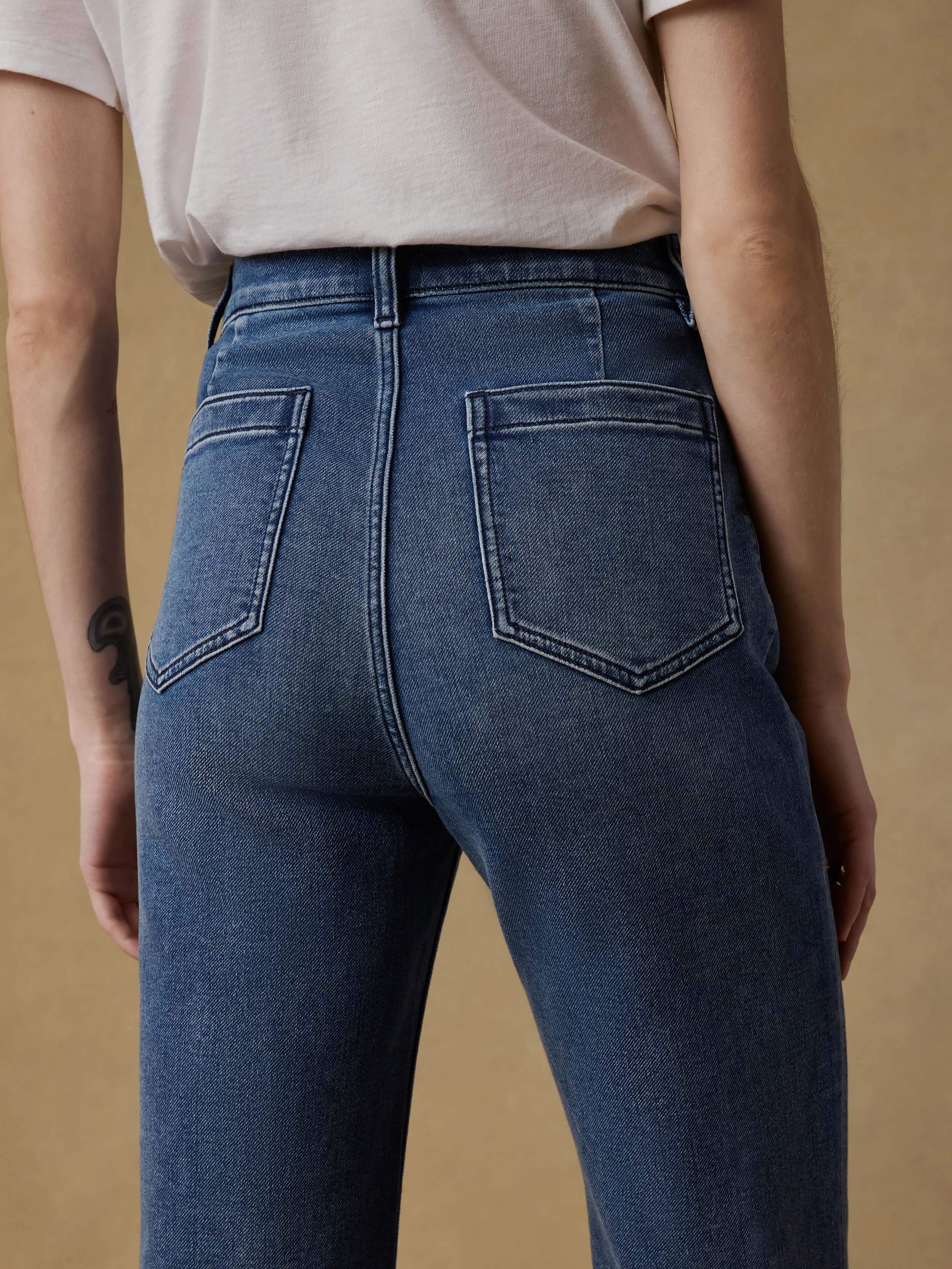 Detail back view of a woman wearing a white t-shirt and blue jeans against a beige background