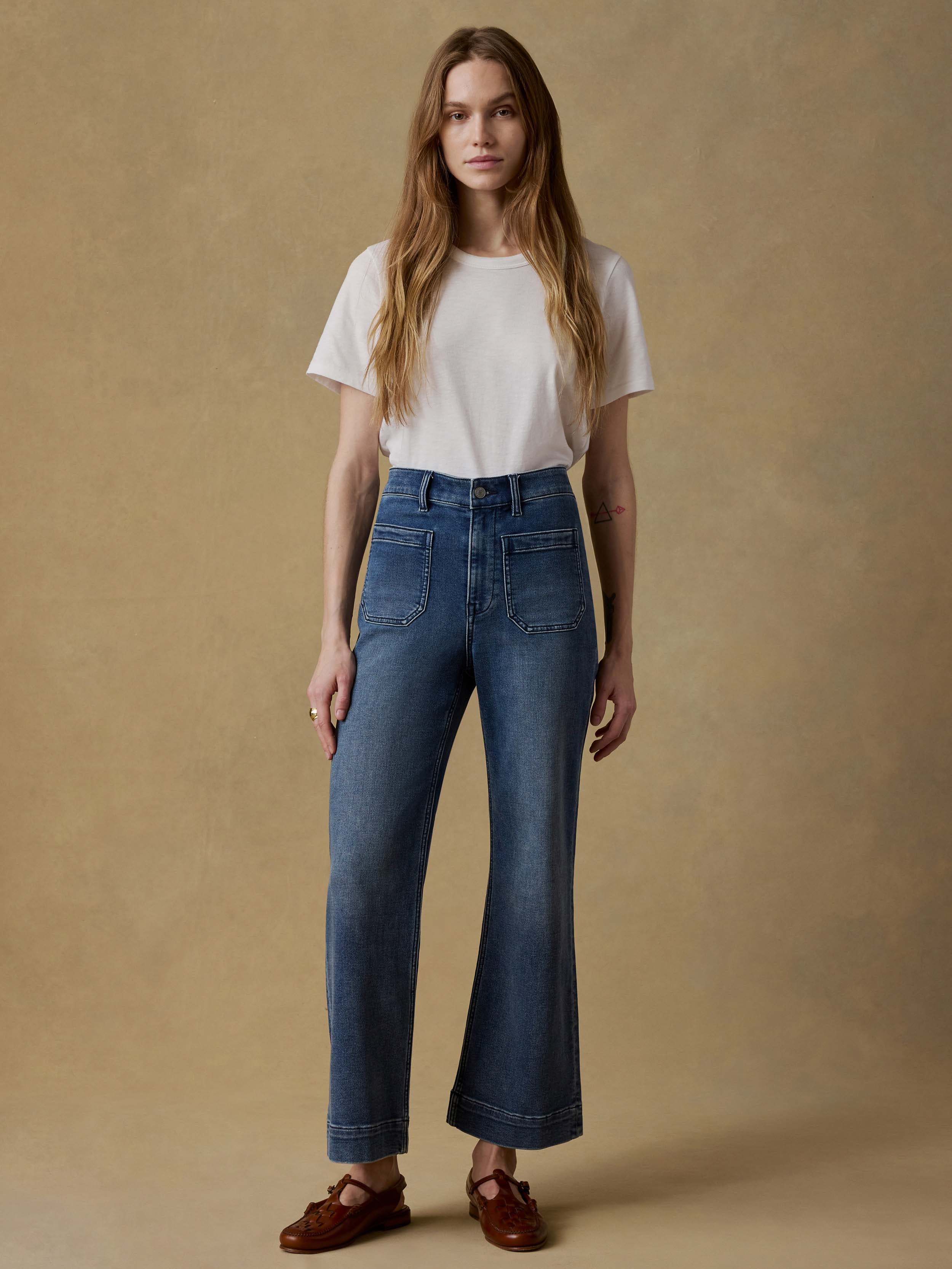 Woman wearing a white t-shirt and blue jeans against a beige background