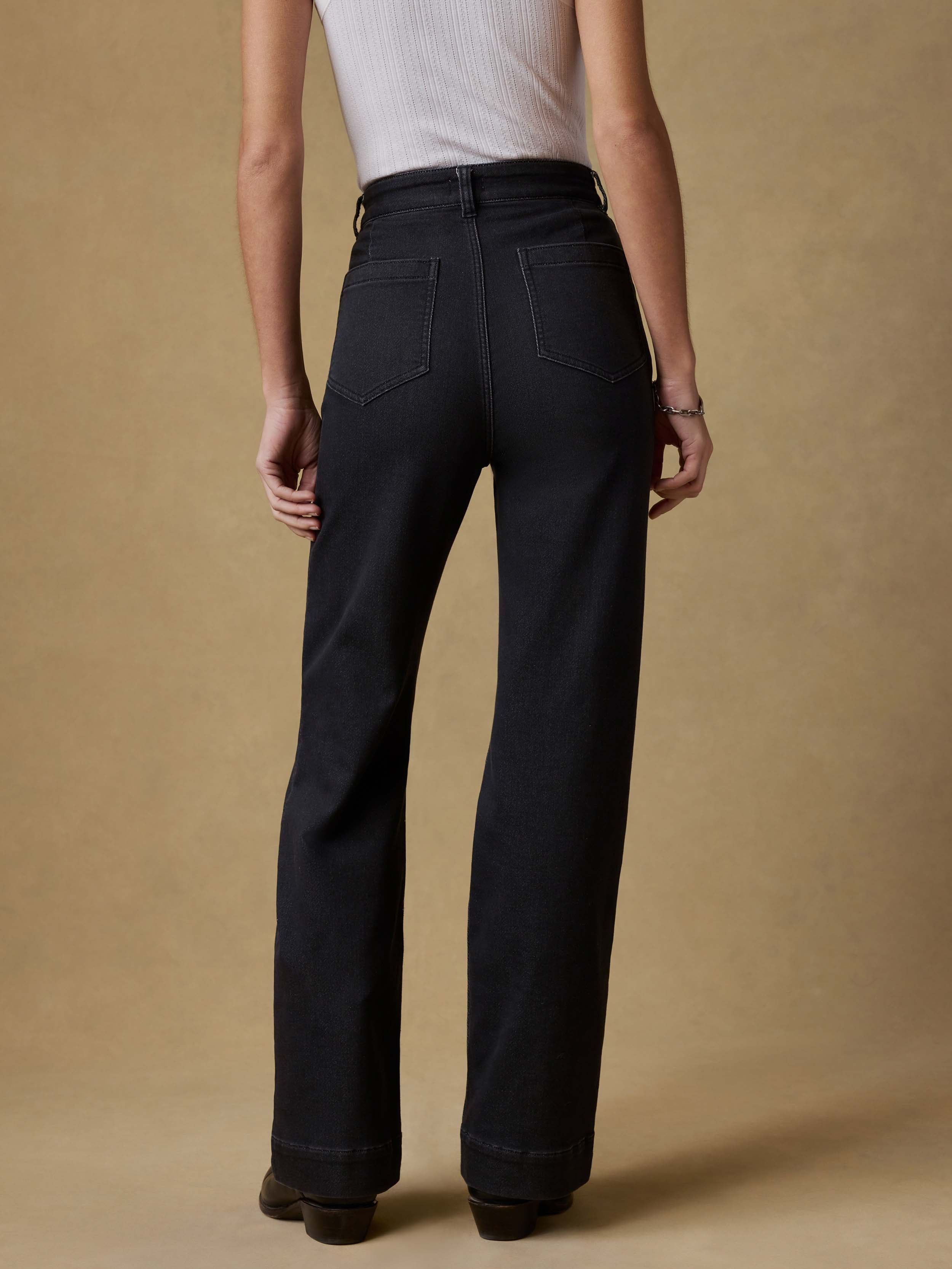 Back view of a woman wearing a white tank top and black pants against a beige background