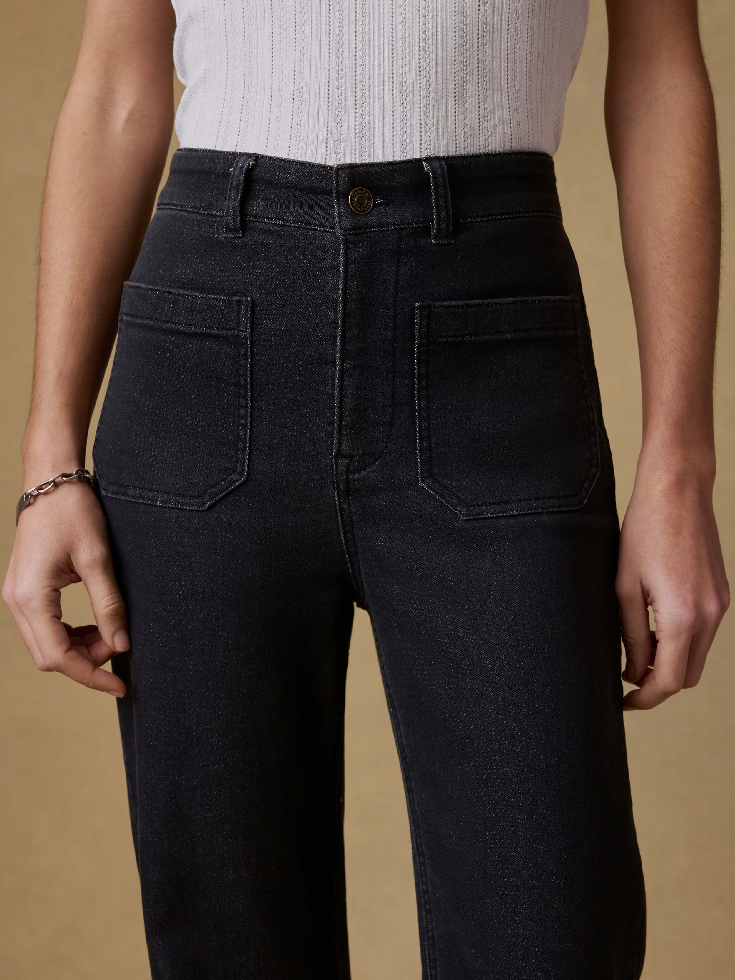 Detail view of a woman wearing a white tank top and black pants against a beige background