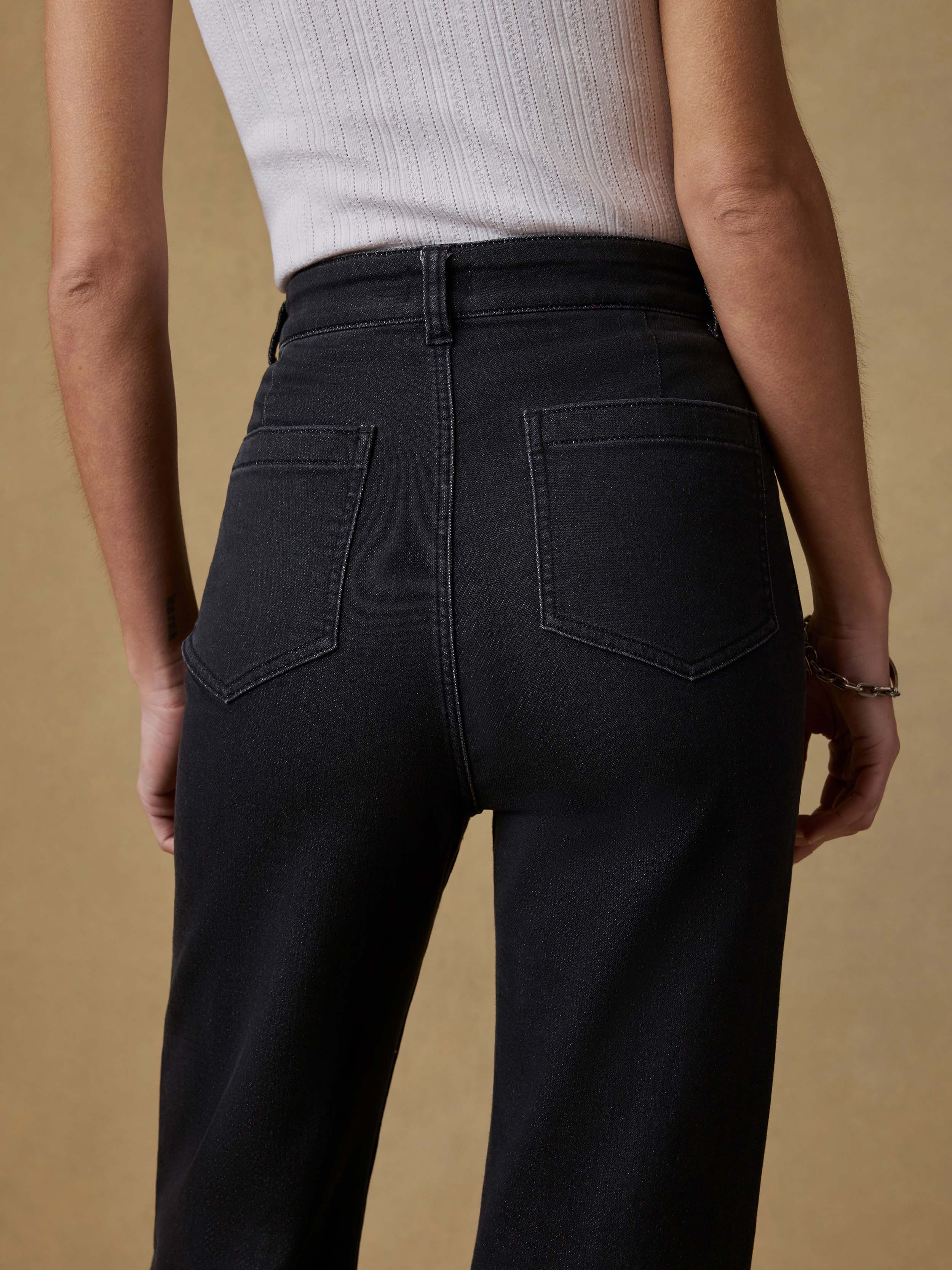 Detail back view of a woman wearing a white tank top and black pants against a beige background