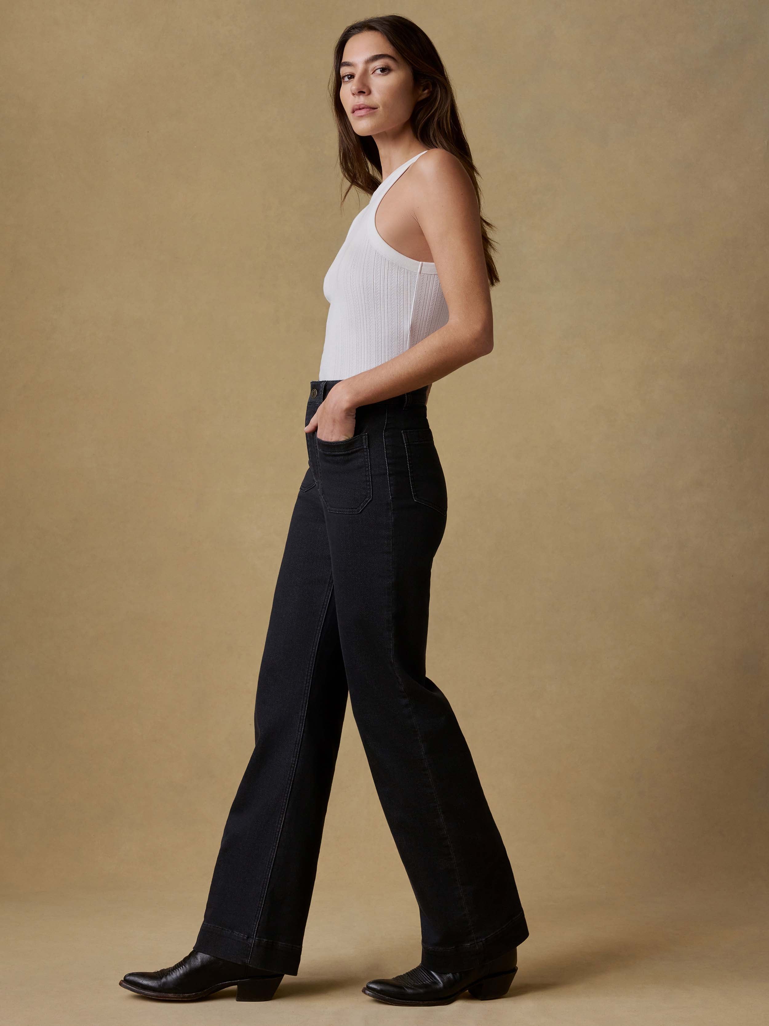 Woman wearing a white tank top and black pants against a beige background