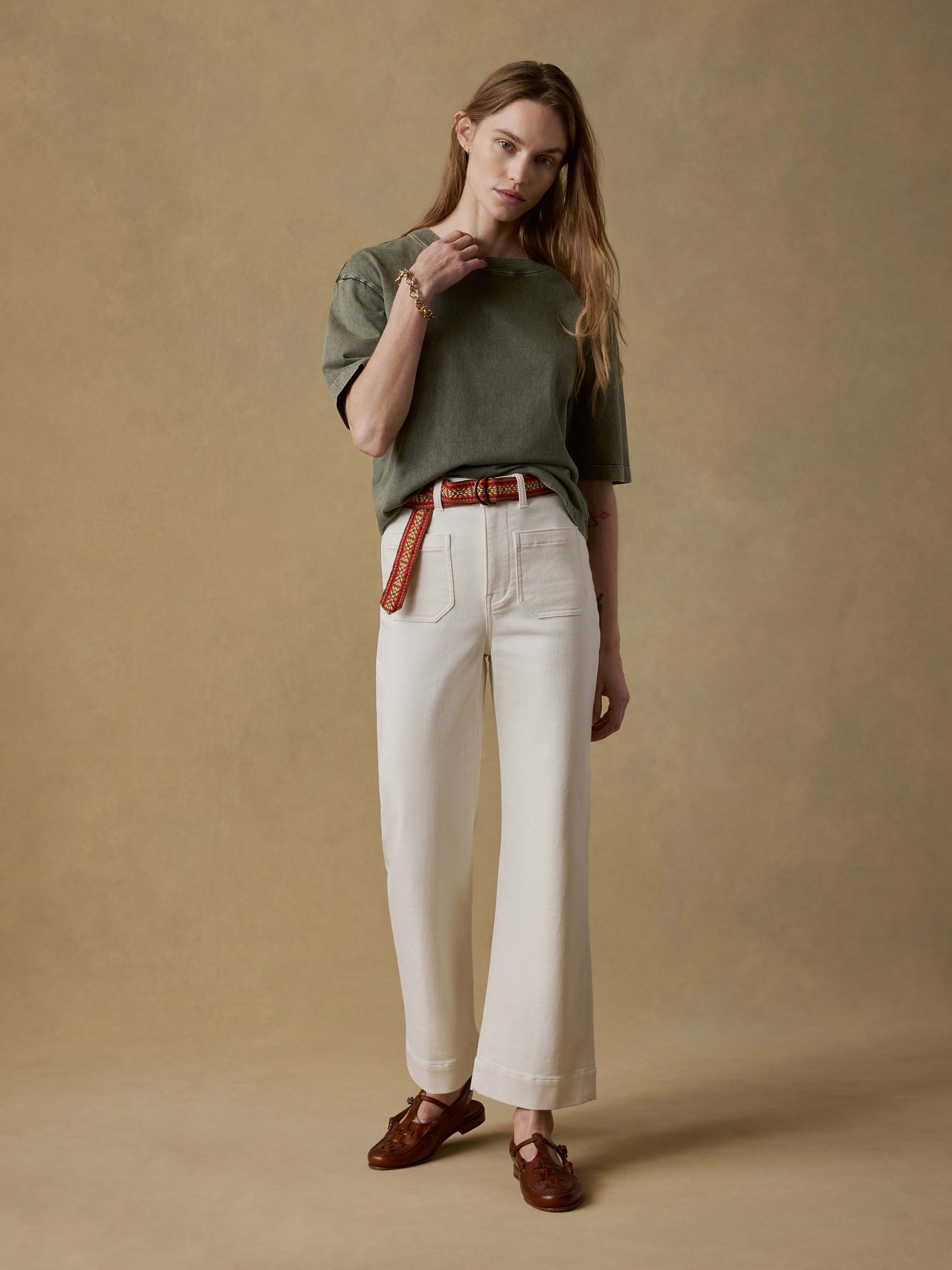 Woman wearing a green t-shirt and white pants against a beige background