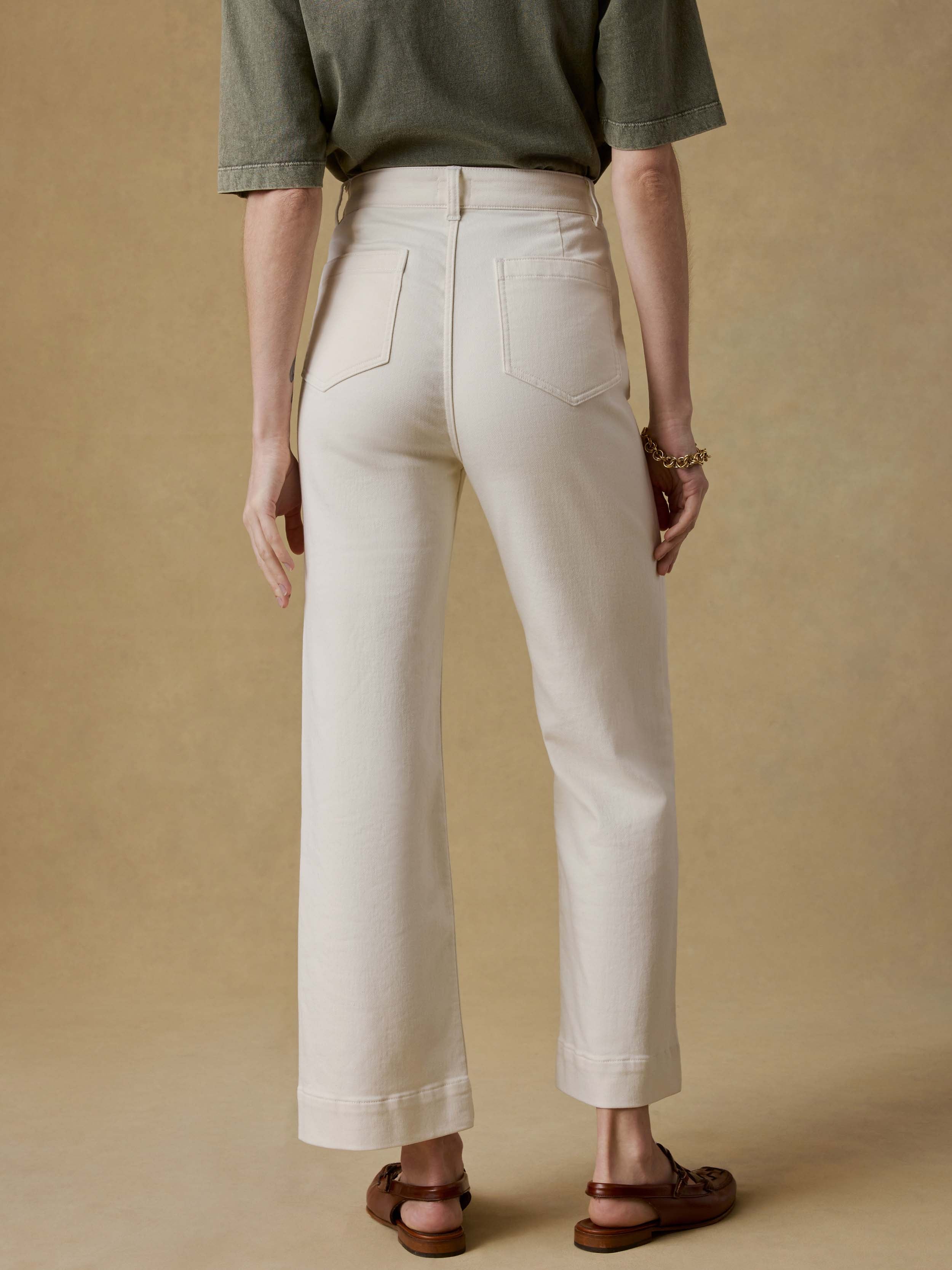 Back view of a woman wearing a green t-shirt and white pants against a beige background