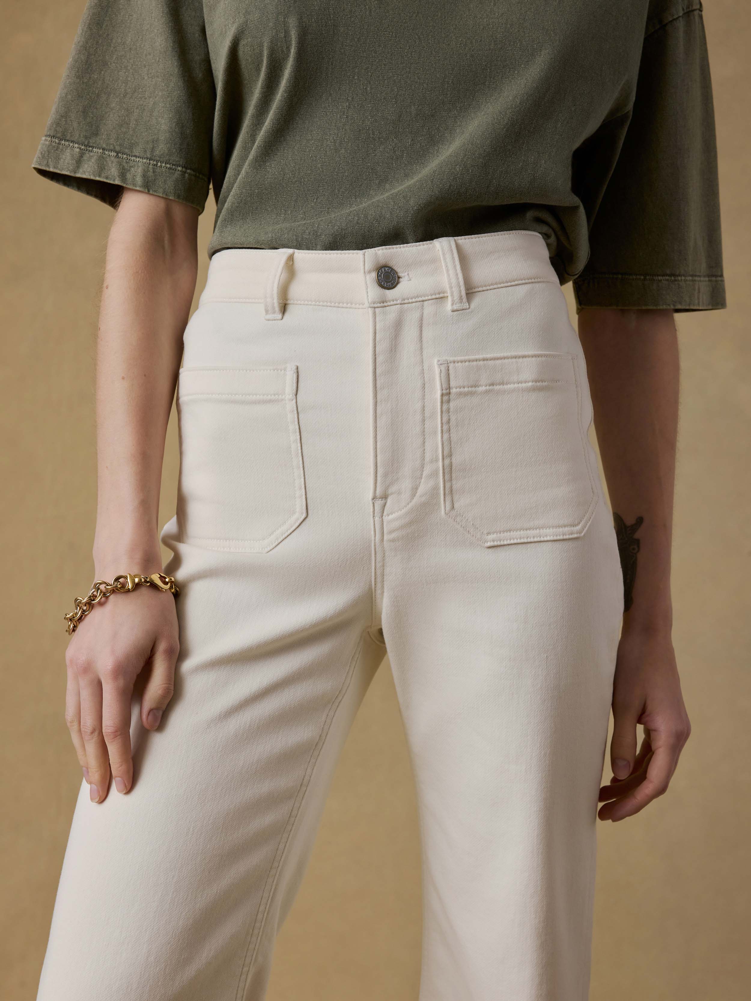 Detail shot of a woman wearing a green t-shirt and white pants against a beige background
