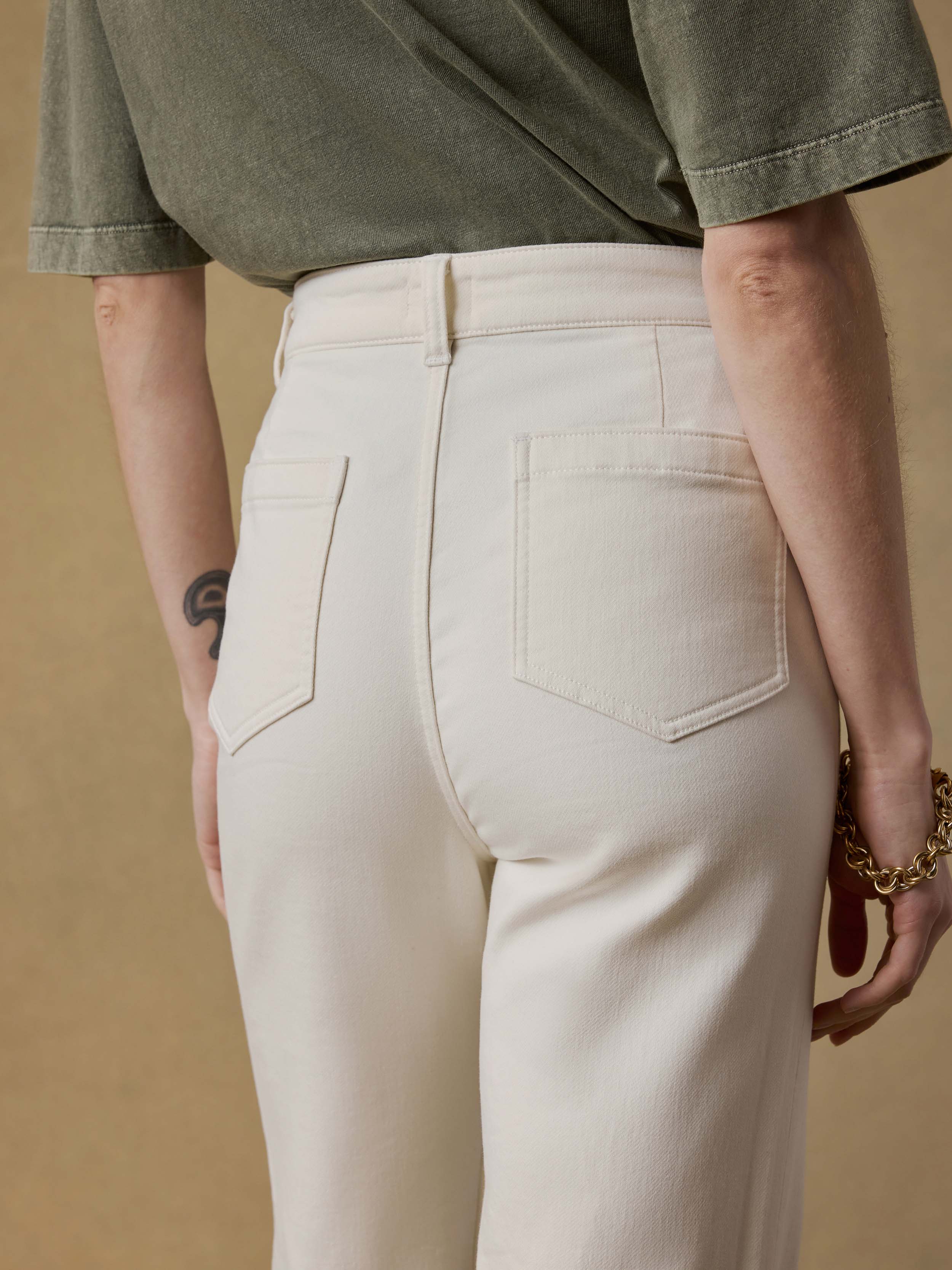 Detail back view of a woman wearing a green t-shirt and white pants against a beige background
