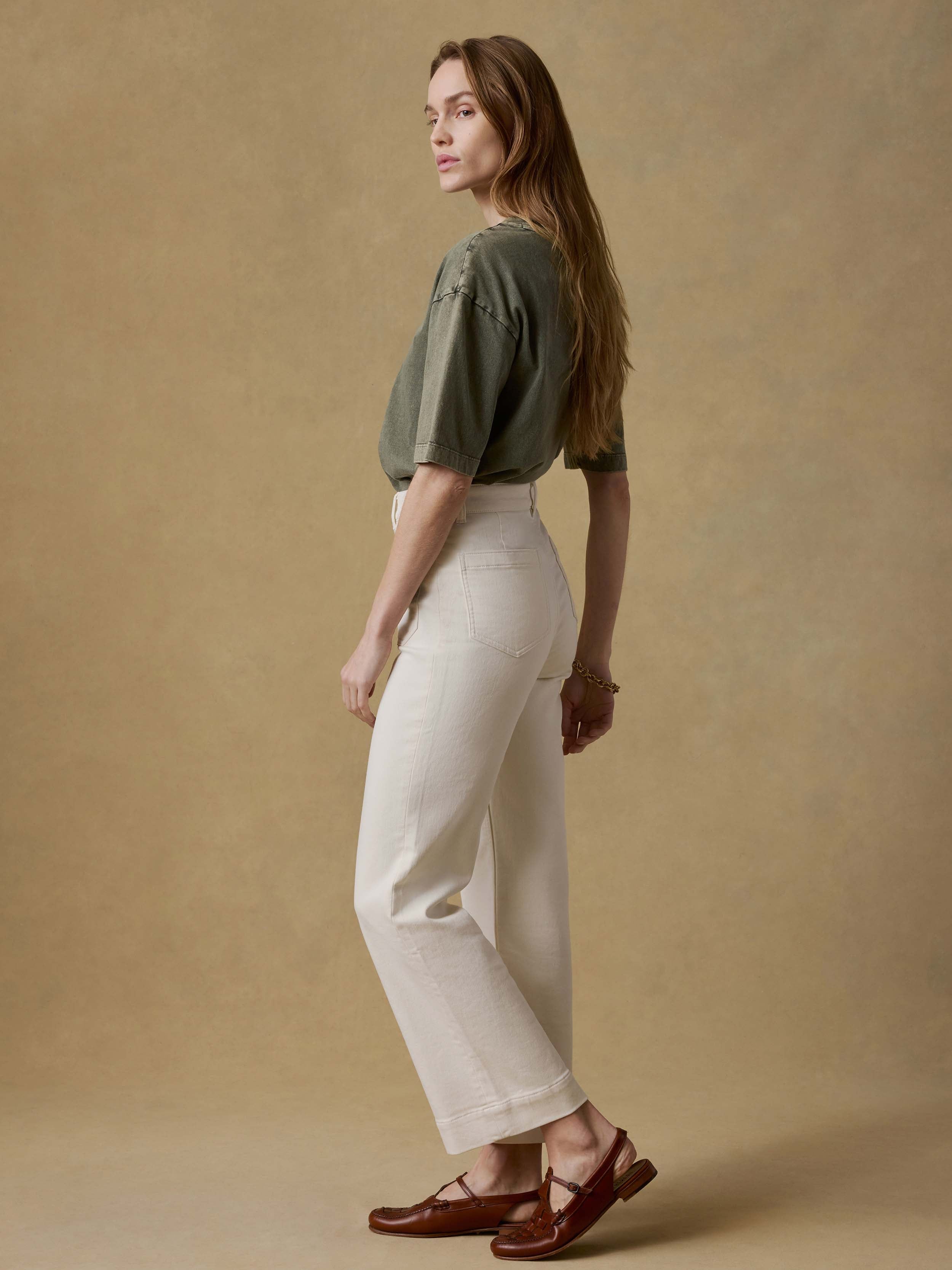 Woman wearing a green t-shirt and white pants against a beige background