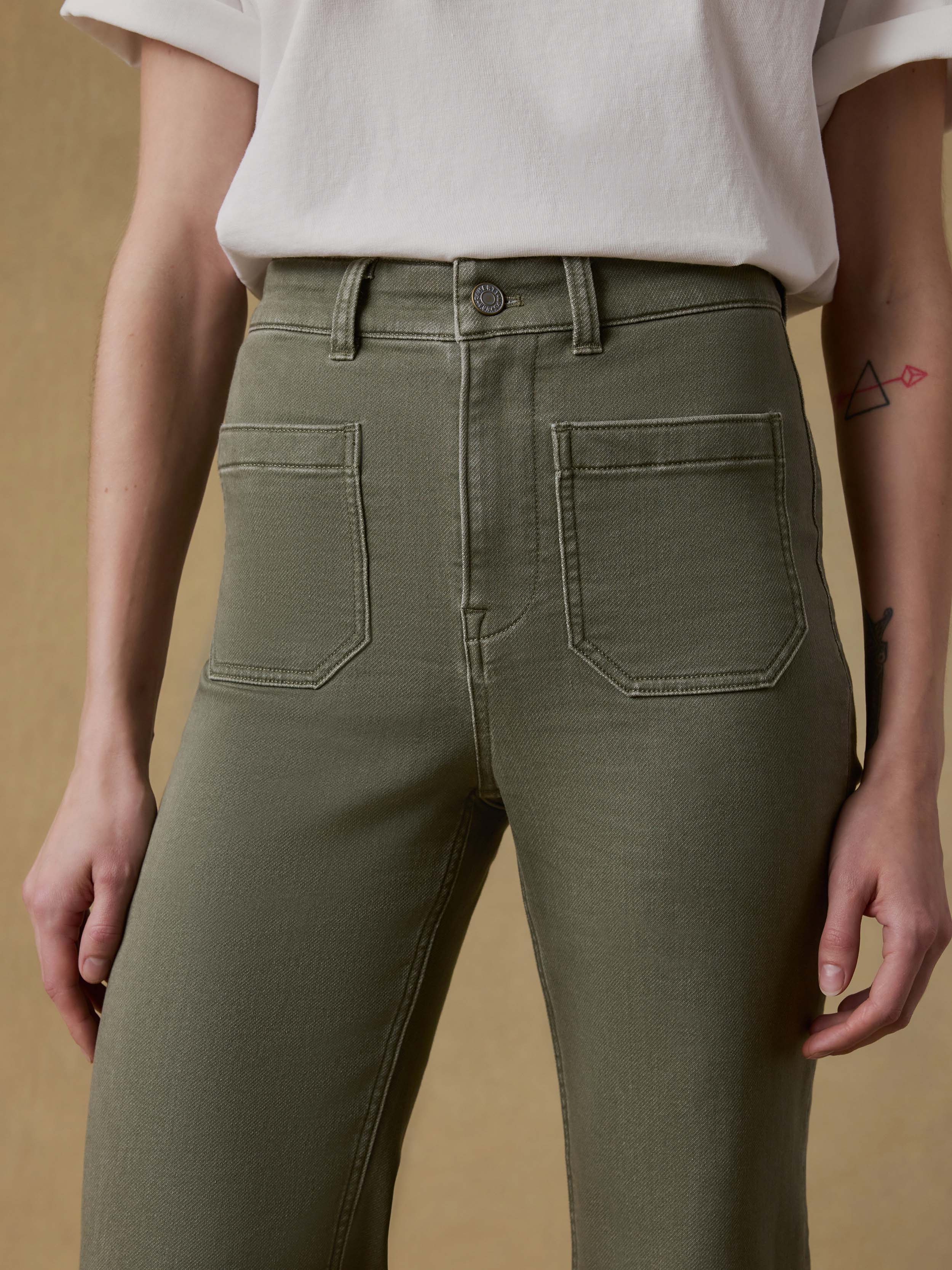 Detail view of a woman wearing a white t-shirt and green pants against a beige background