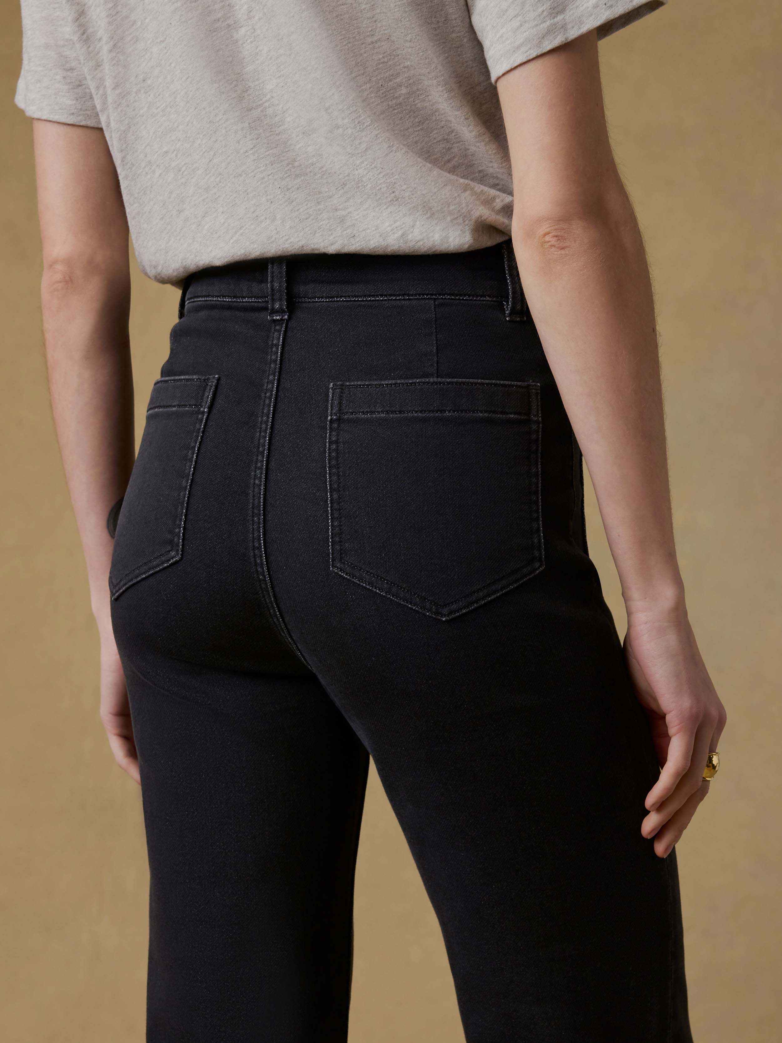 Back view of a woman wearing a light gray t-shirt and black pants against a beige background