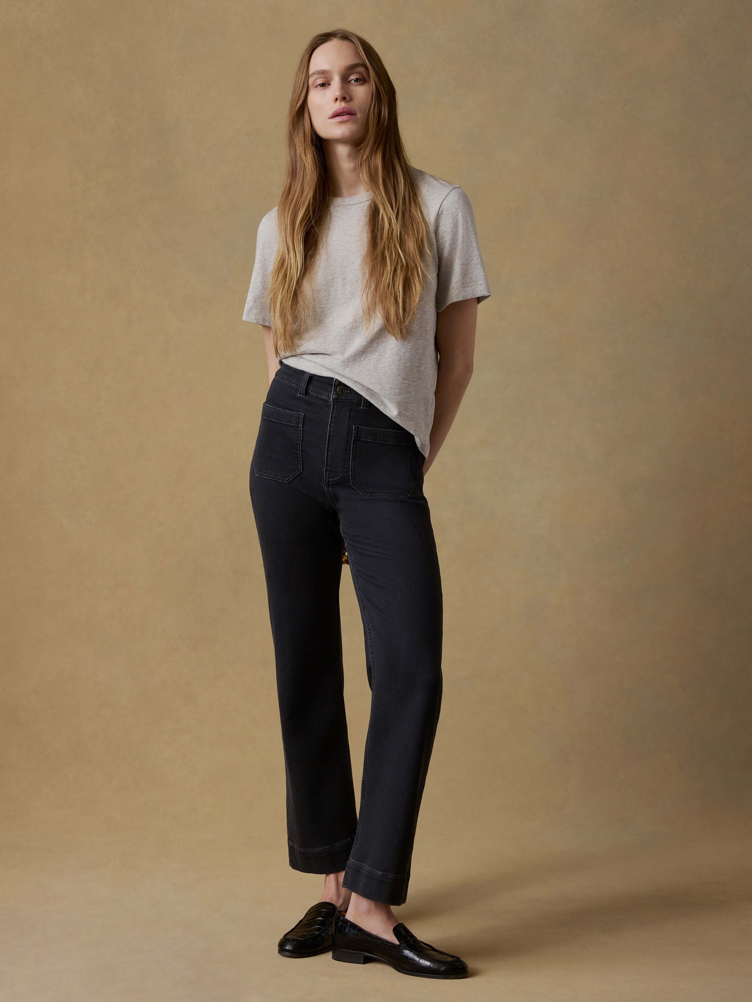 Woman wearing a light gray t-shirt and black pants against a beige background