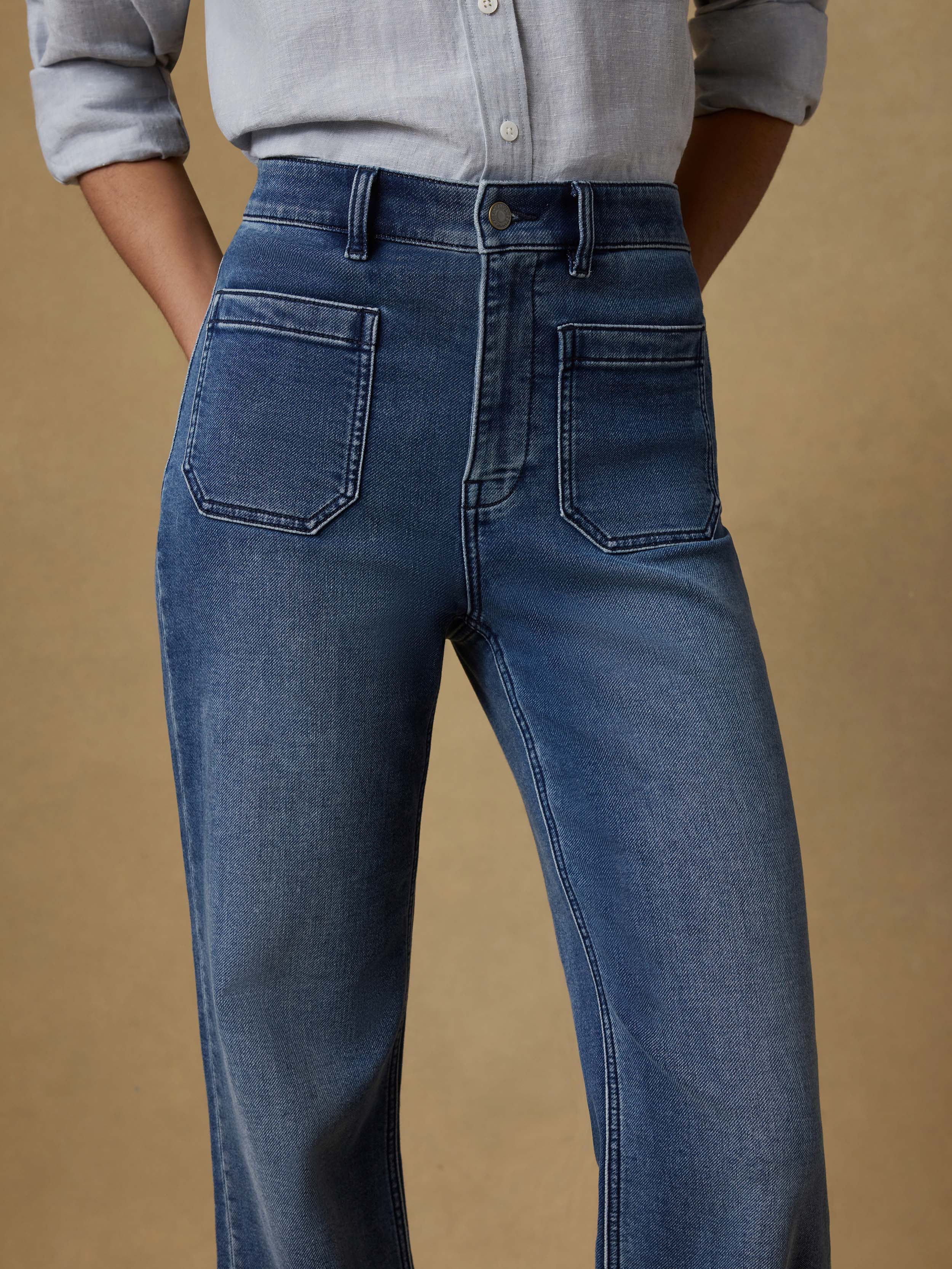 Detail view of a woman wearing a light blue button up shirt and dark blue jeans against a beige background