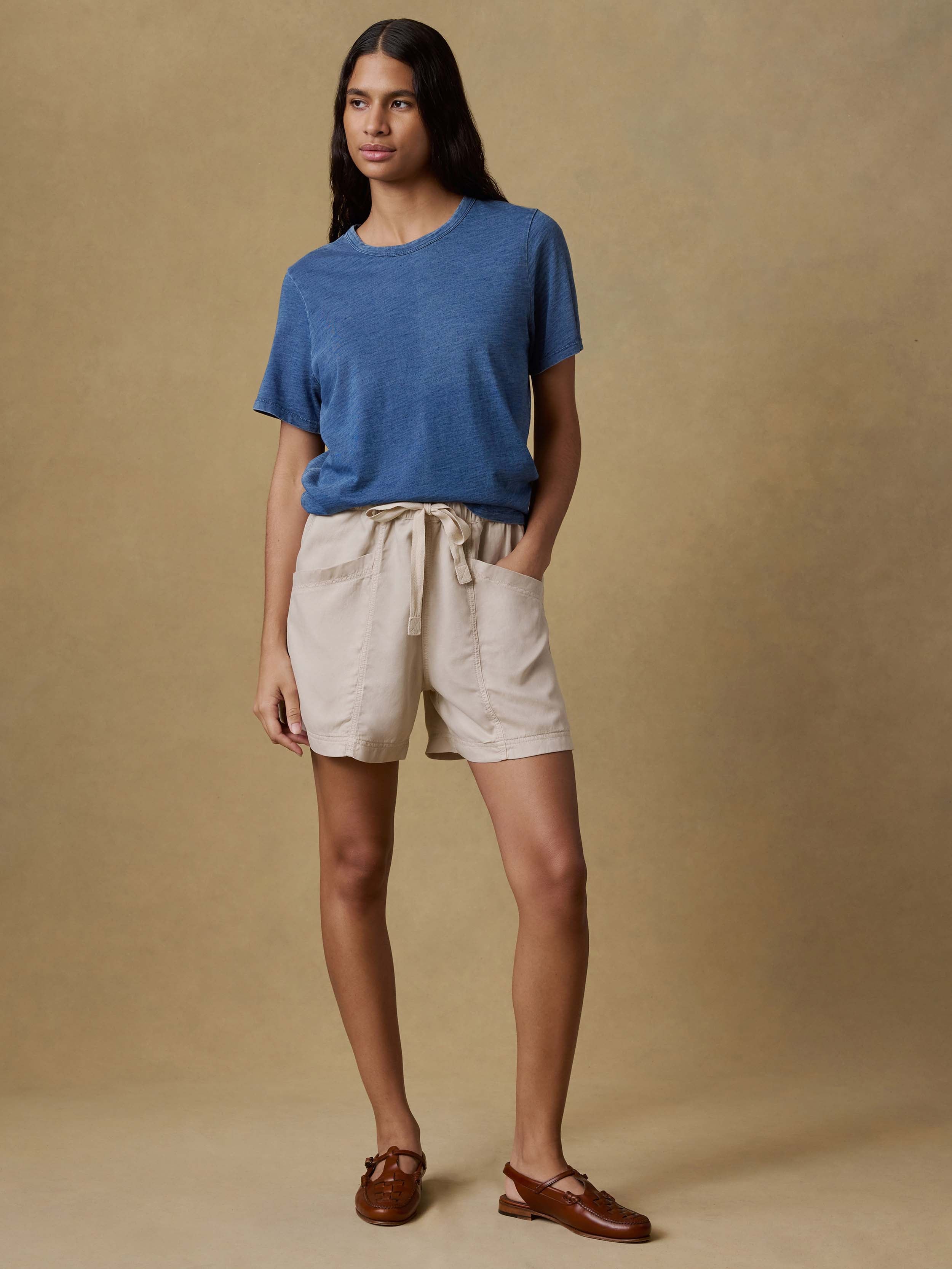 Woman wearing a blue t-shirt and beige shorts against a beige background