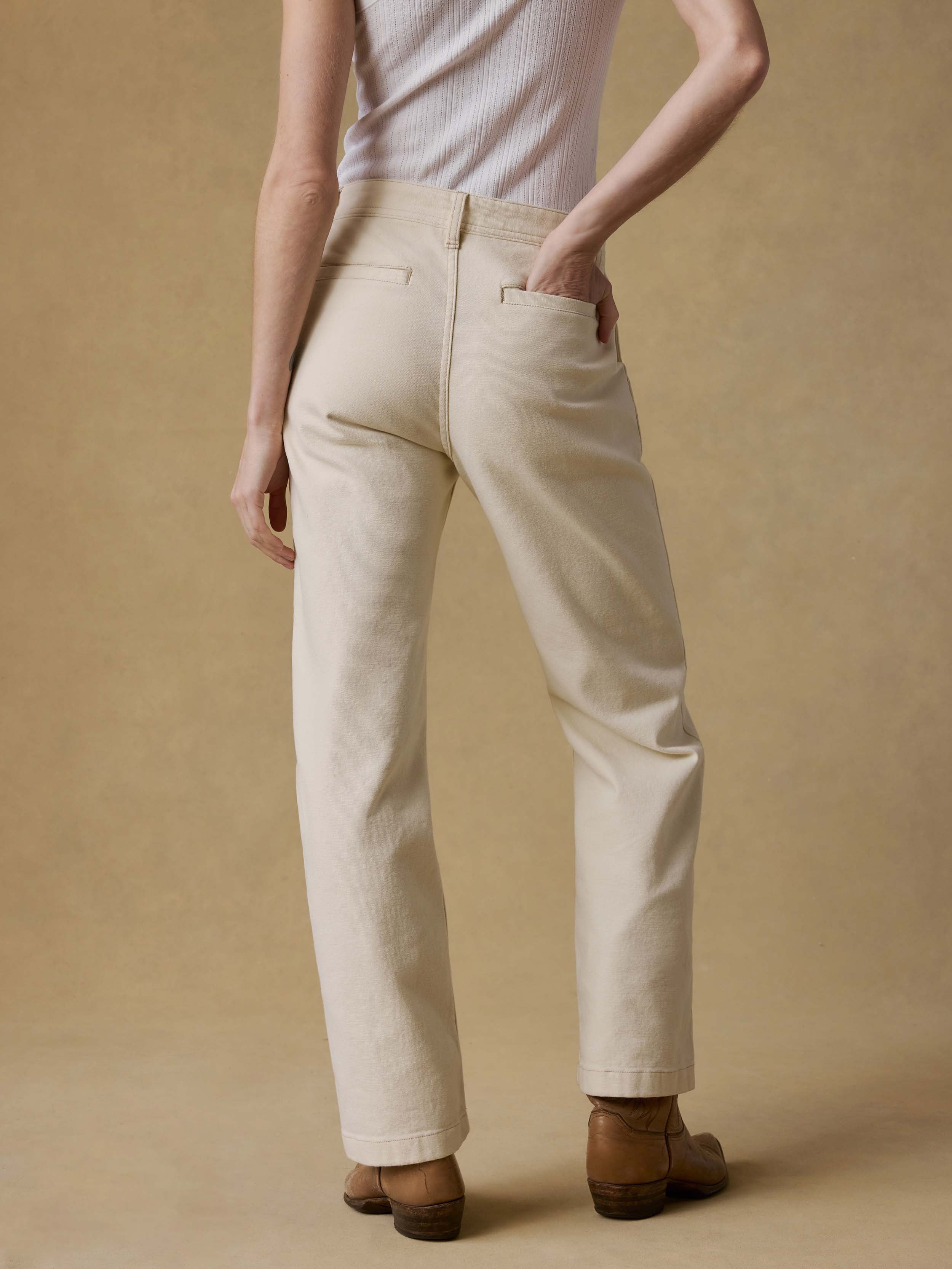 Woman wearing a white tank top, beige pants, and brown shoes on a beige background