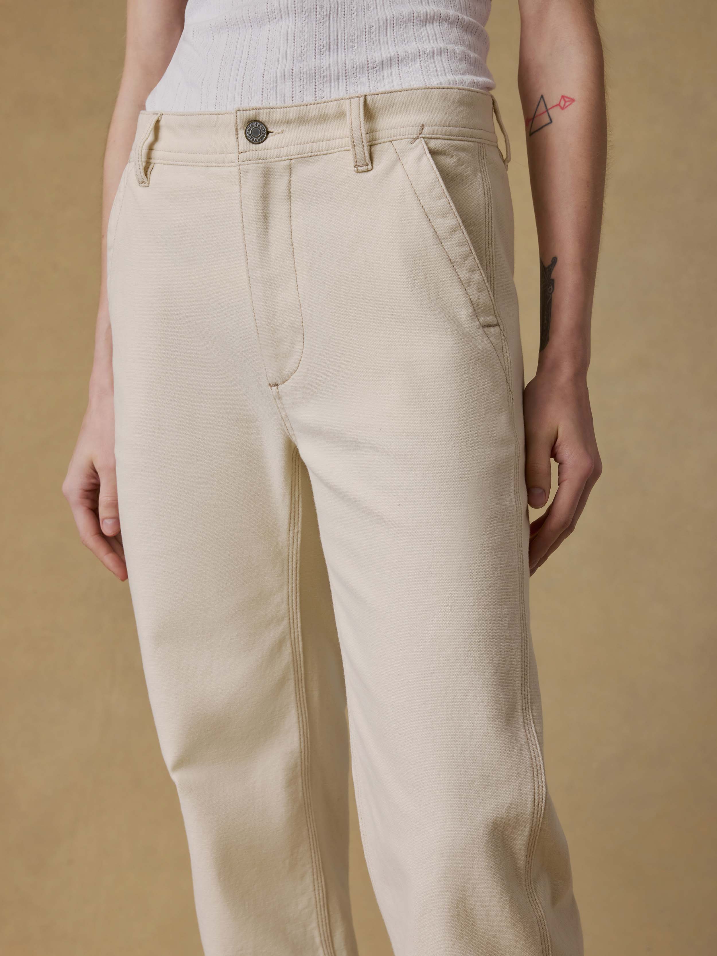 Detail shot of a woman wearing a white tank top and beige pants against a beige background