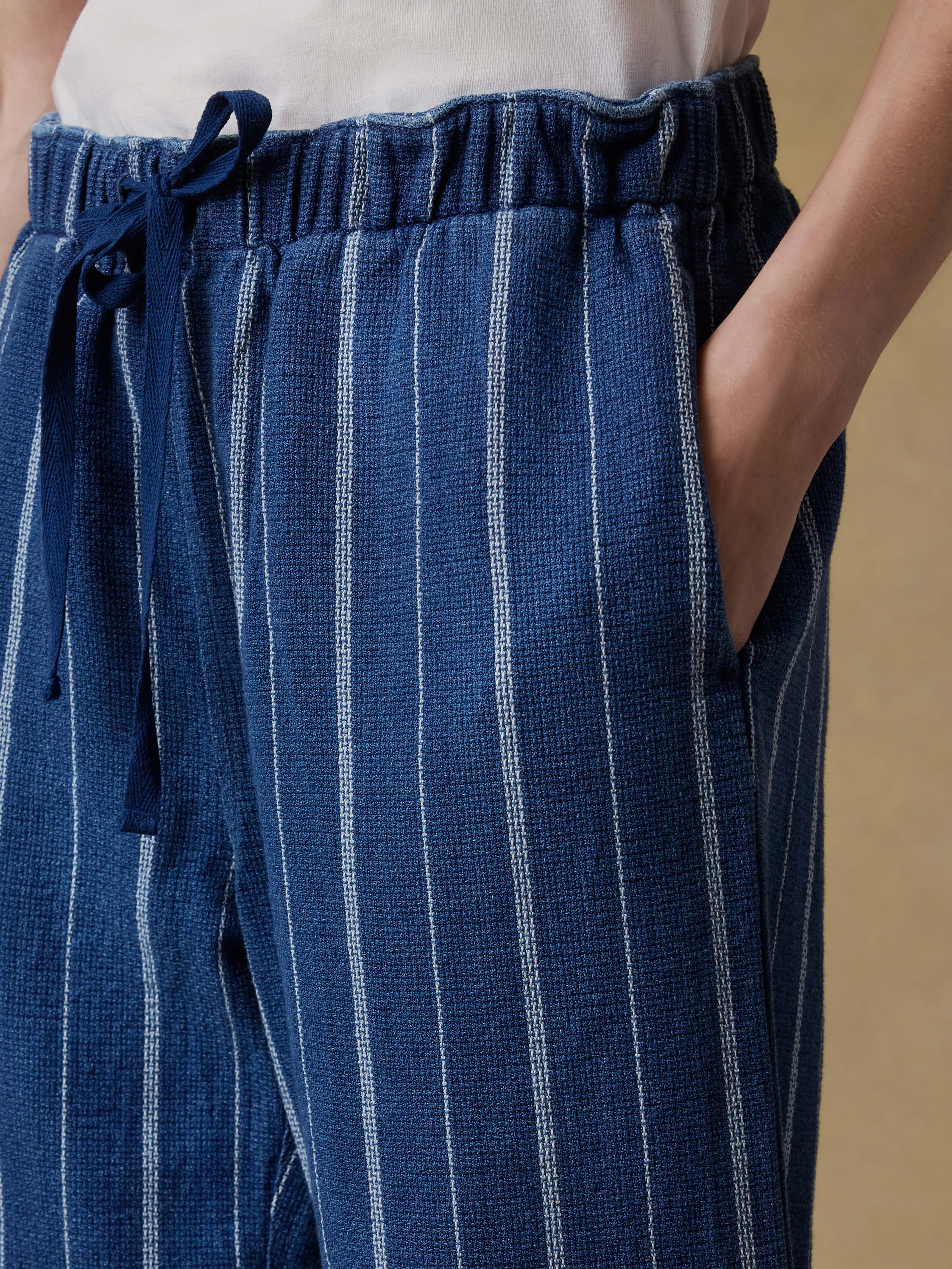 Woman wearing a white top and blue striped pants against a beige background