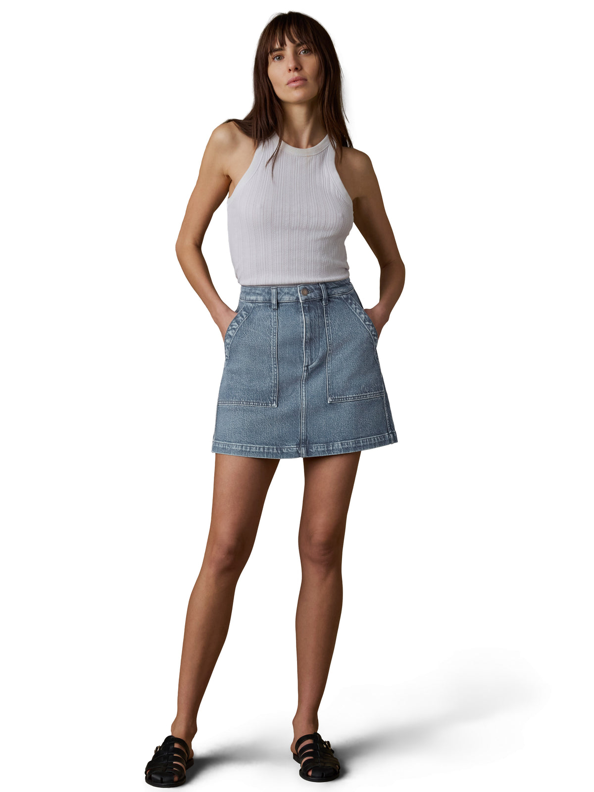 A woman wearing a white tank top, denim skirt, and black sandals, image 1 of 3