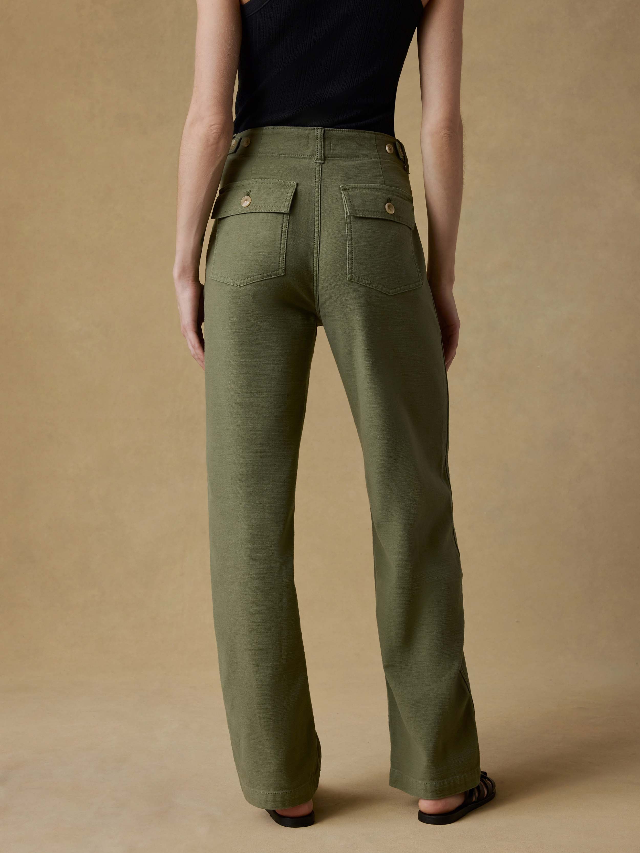 Back view of a woman wearing a black tank top and green pants against a beige background