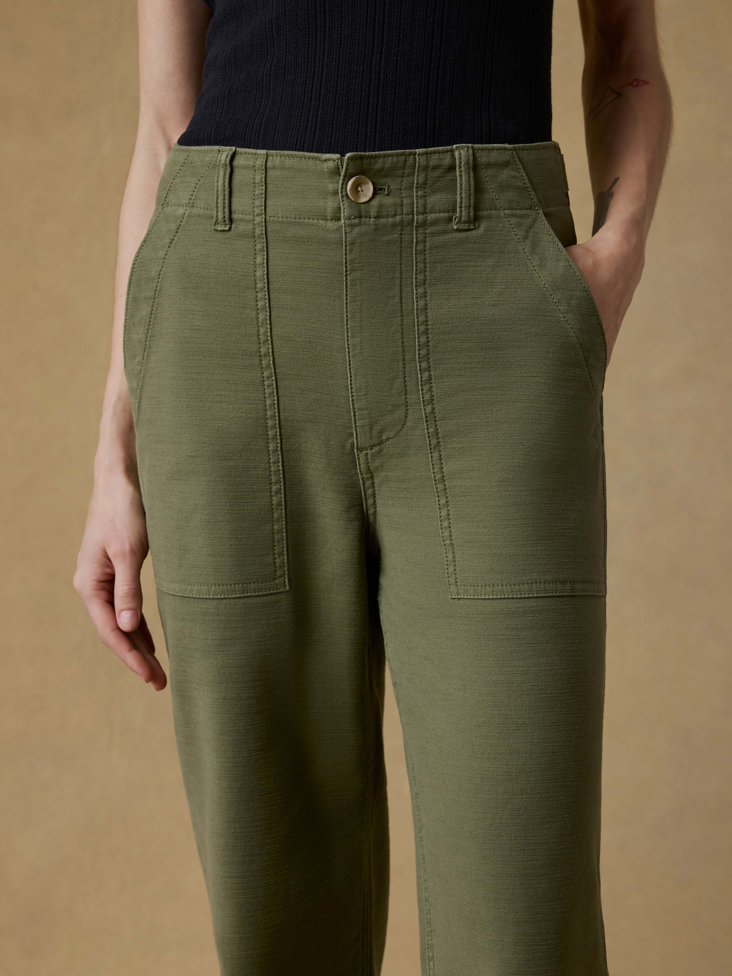 Woman wearing a black tank top and green pants against a beige background