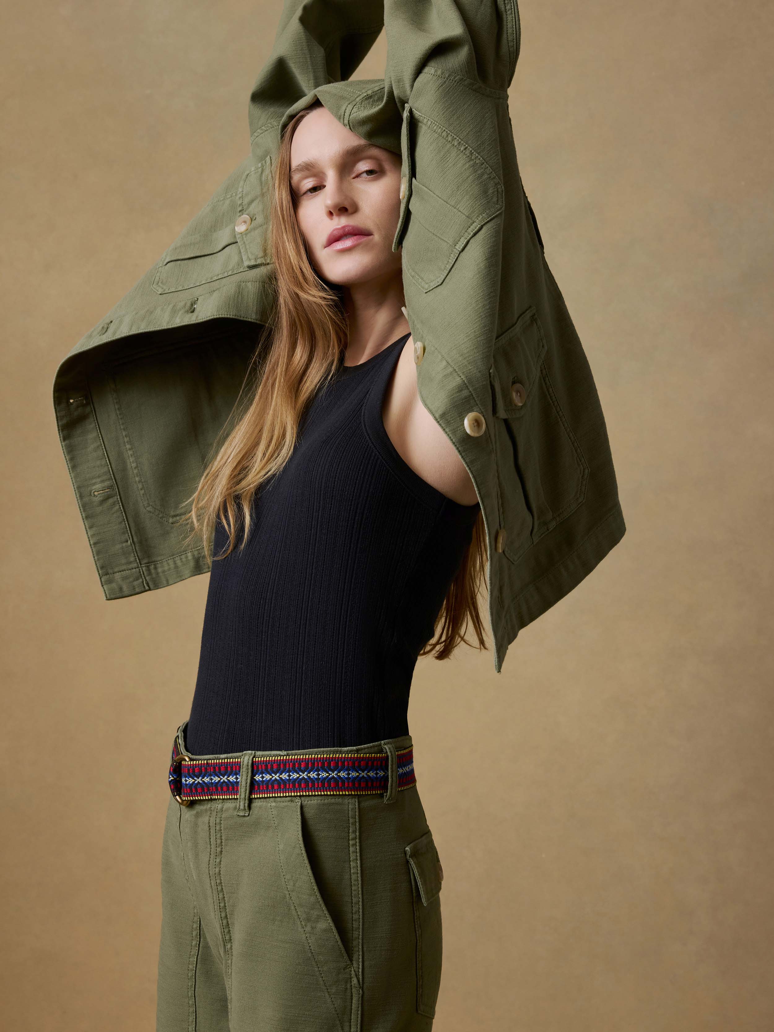 Woman wearing a green jacket over a black tank top and green pants against a beige background