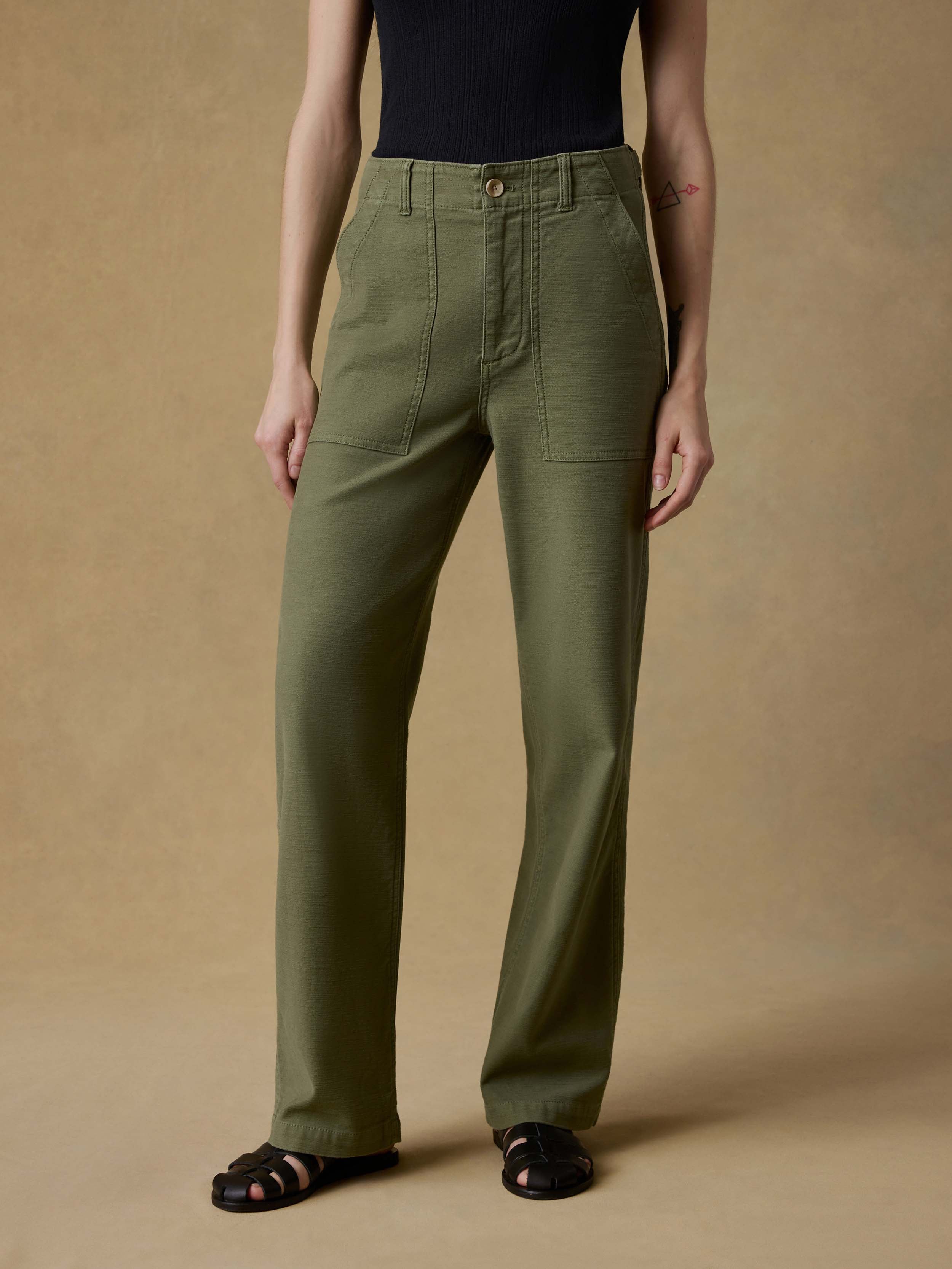 Woman wearing a black tank top and green pants against a beige background