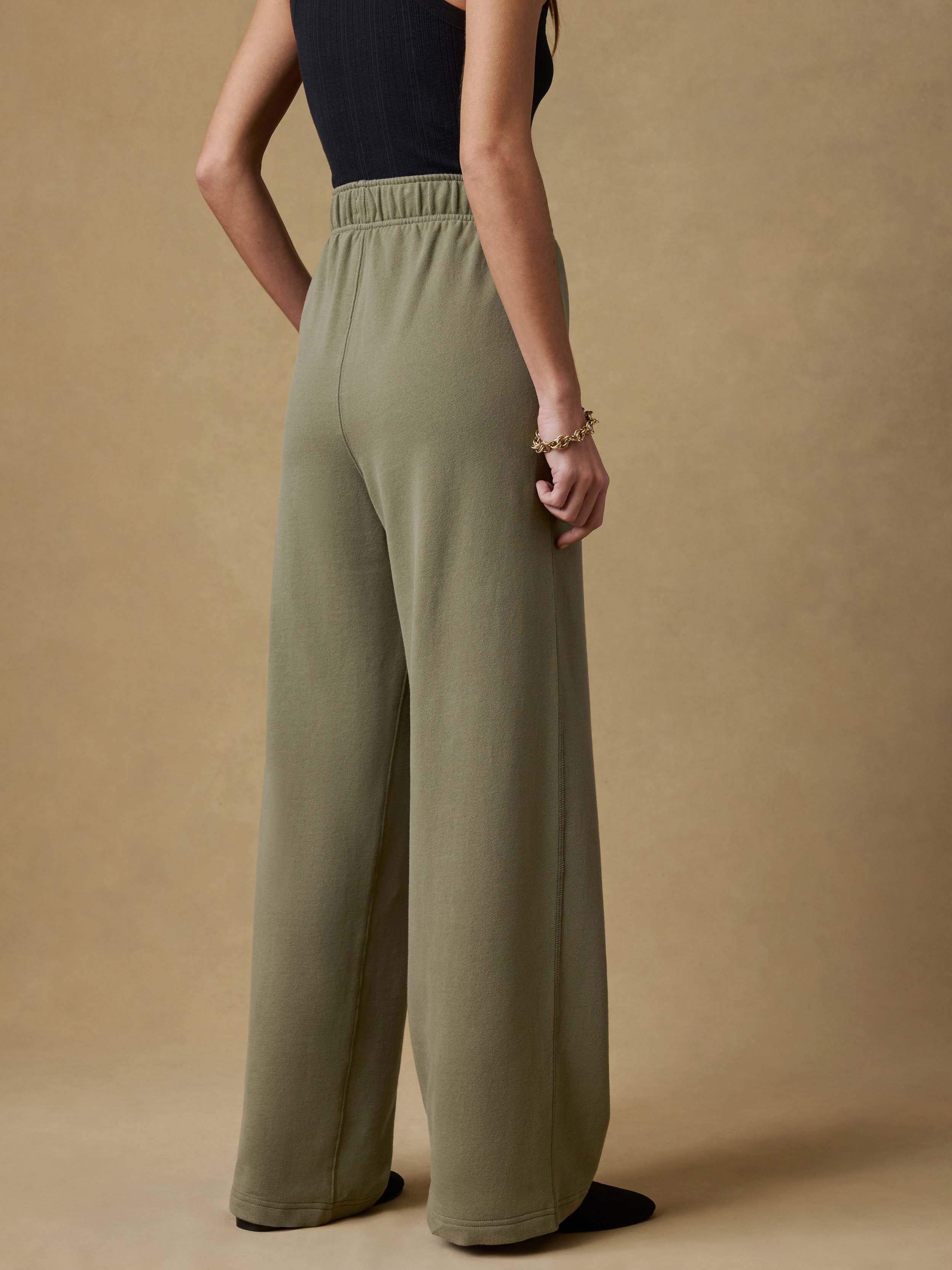 Back view of a woman wearing a black tank top and green wide-leg sweatpants against a beige background