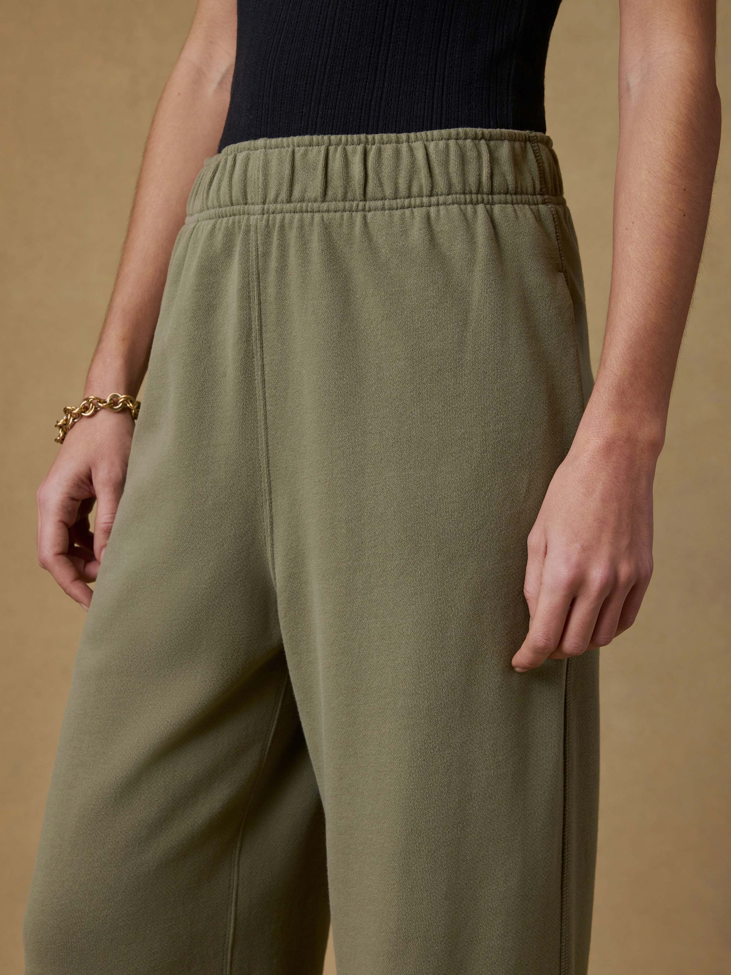 Woman wearing a black tank top and green wide-leg sweatpants against a beige background