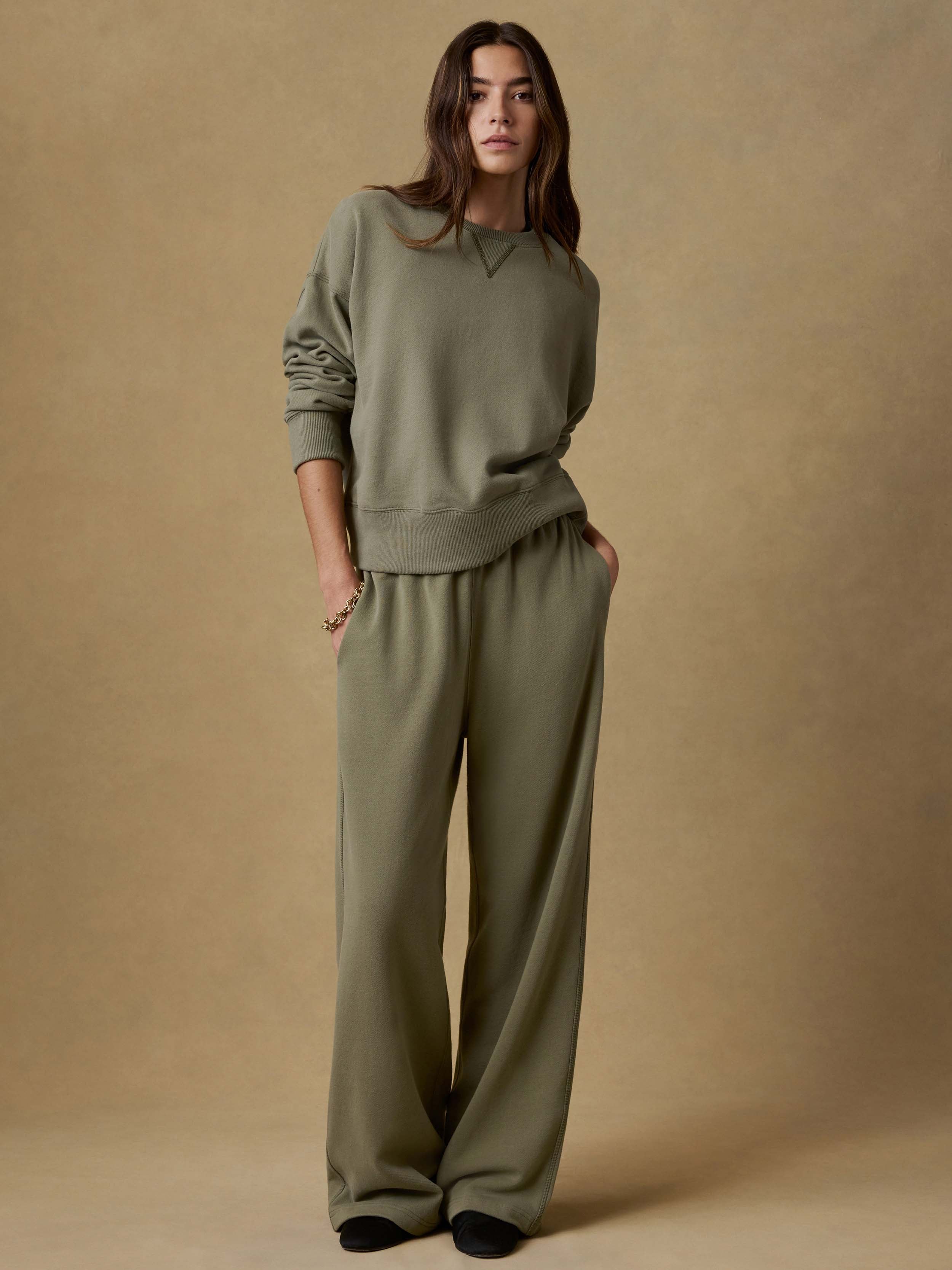 Woman wearing a green sweatshirt and matching green wide-leg sweatpants against a beige background