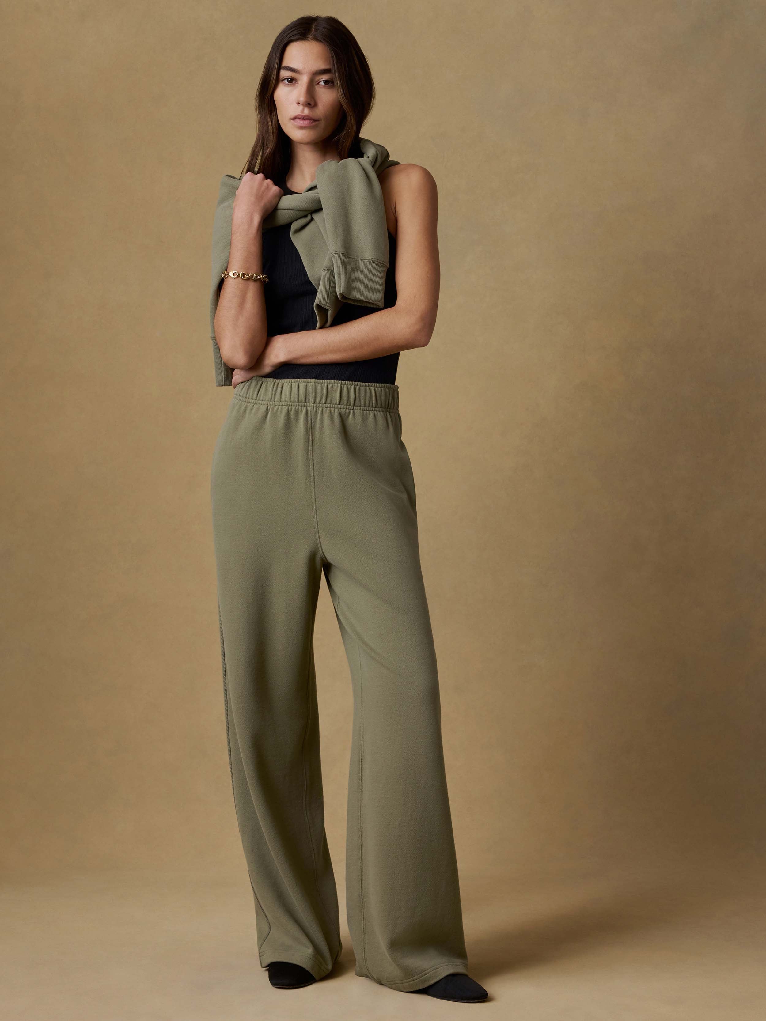 Woman wearing a green top and green wide-leg sweatpants against a beige background