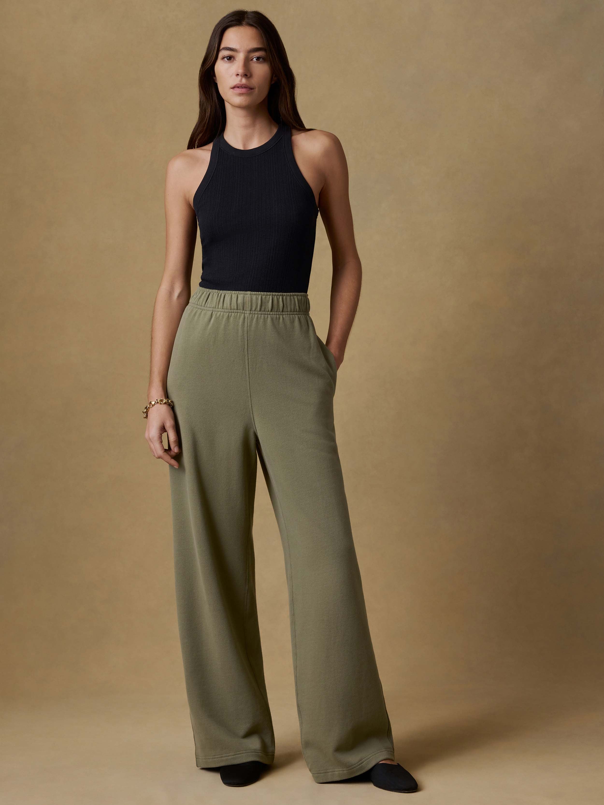 Woman wearing a black tank top and green wide-leg sweatpants against a beige background