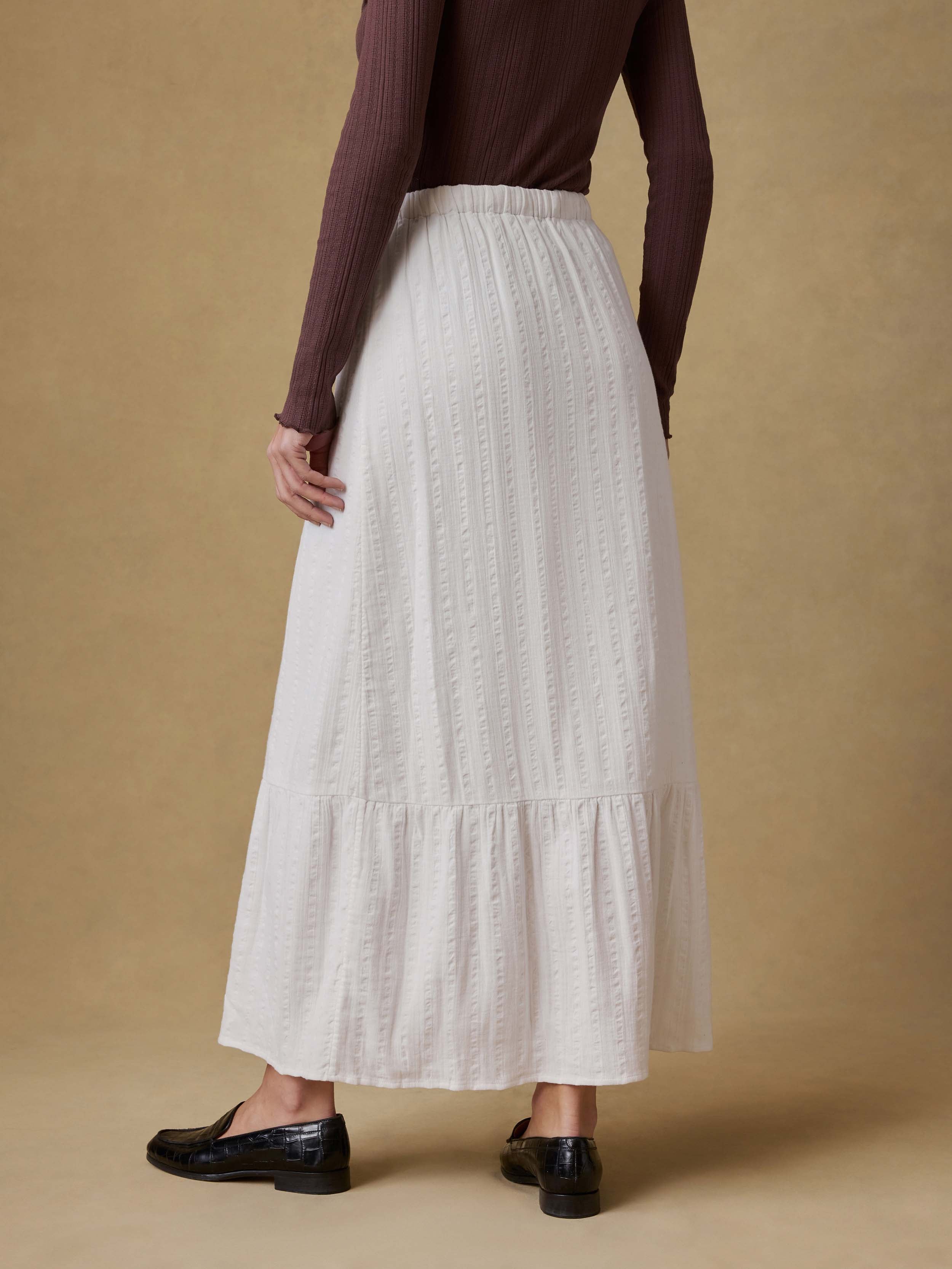 Back view of a woman wearing a brown cardigan and white skirt against a beige background