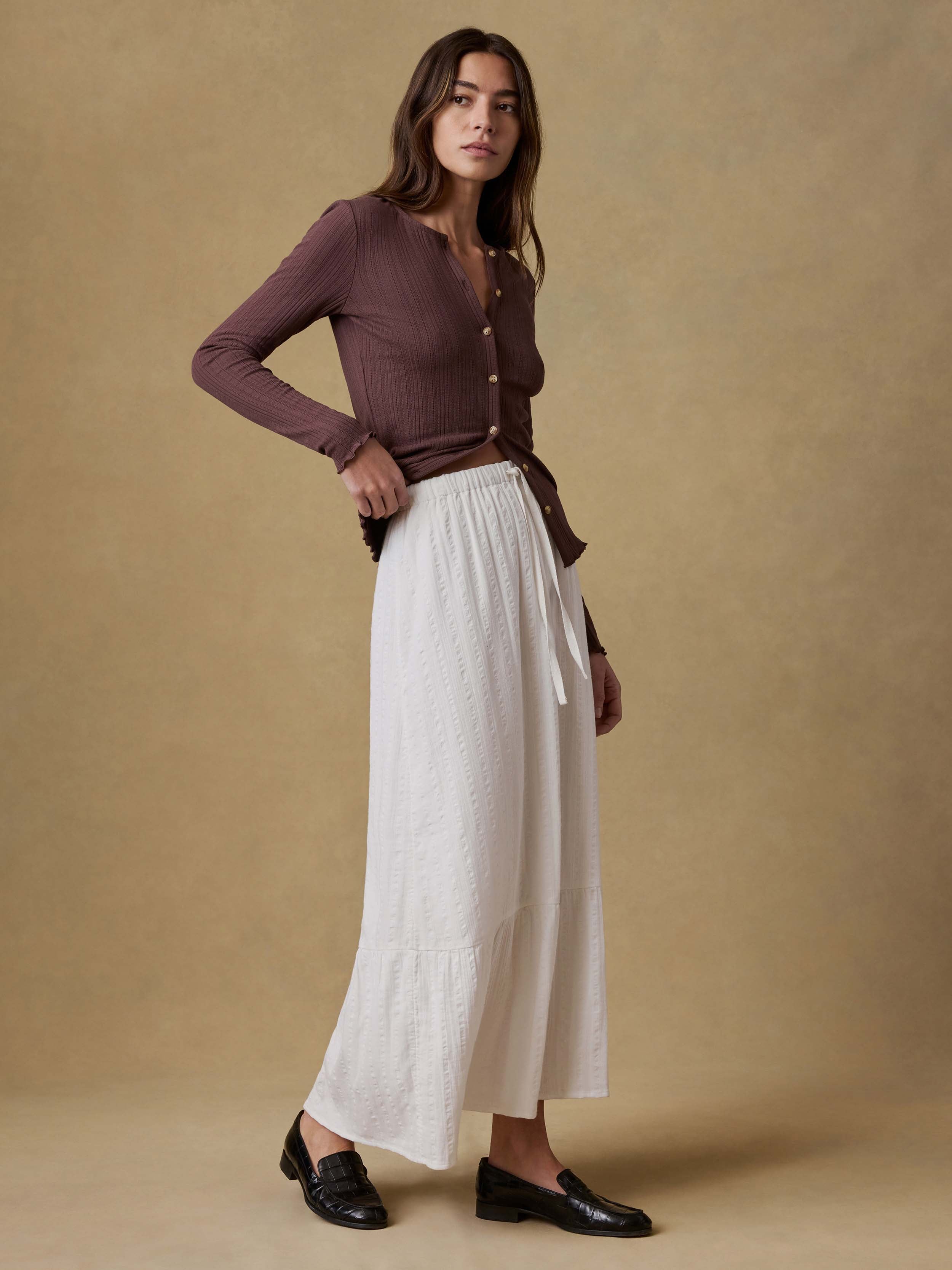 Woman wearing a brown cardigan and white skirt against a beige background
