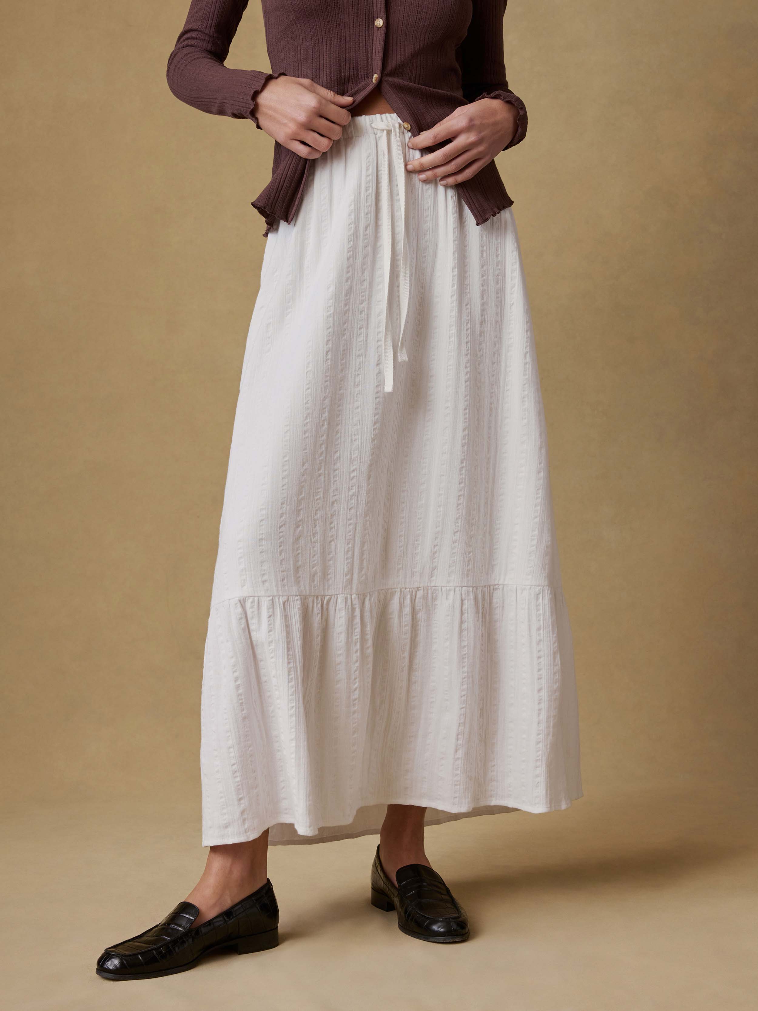 Woman wearing a brown cardigan and white skirt against a beige background