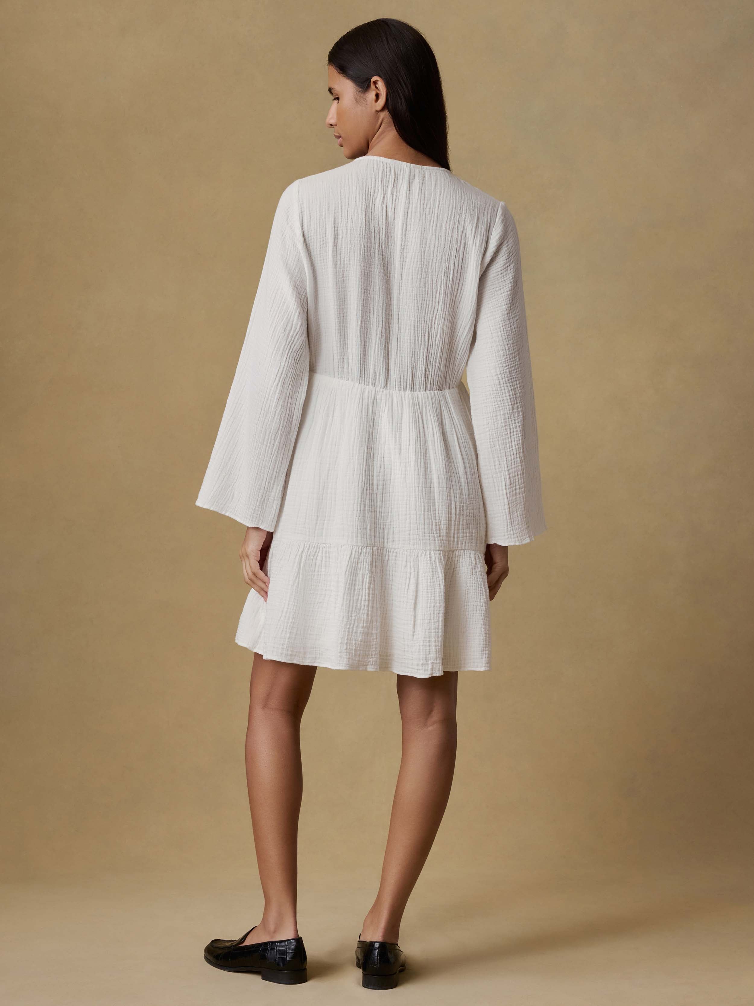 Back view of a woman wearing a white dress against a beige background