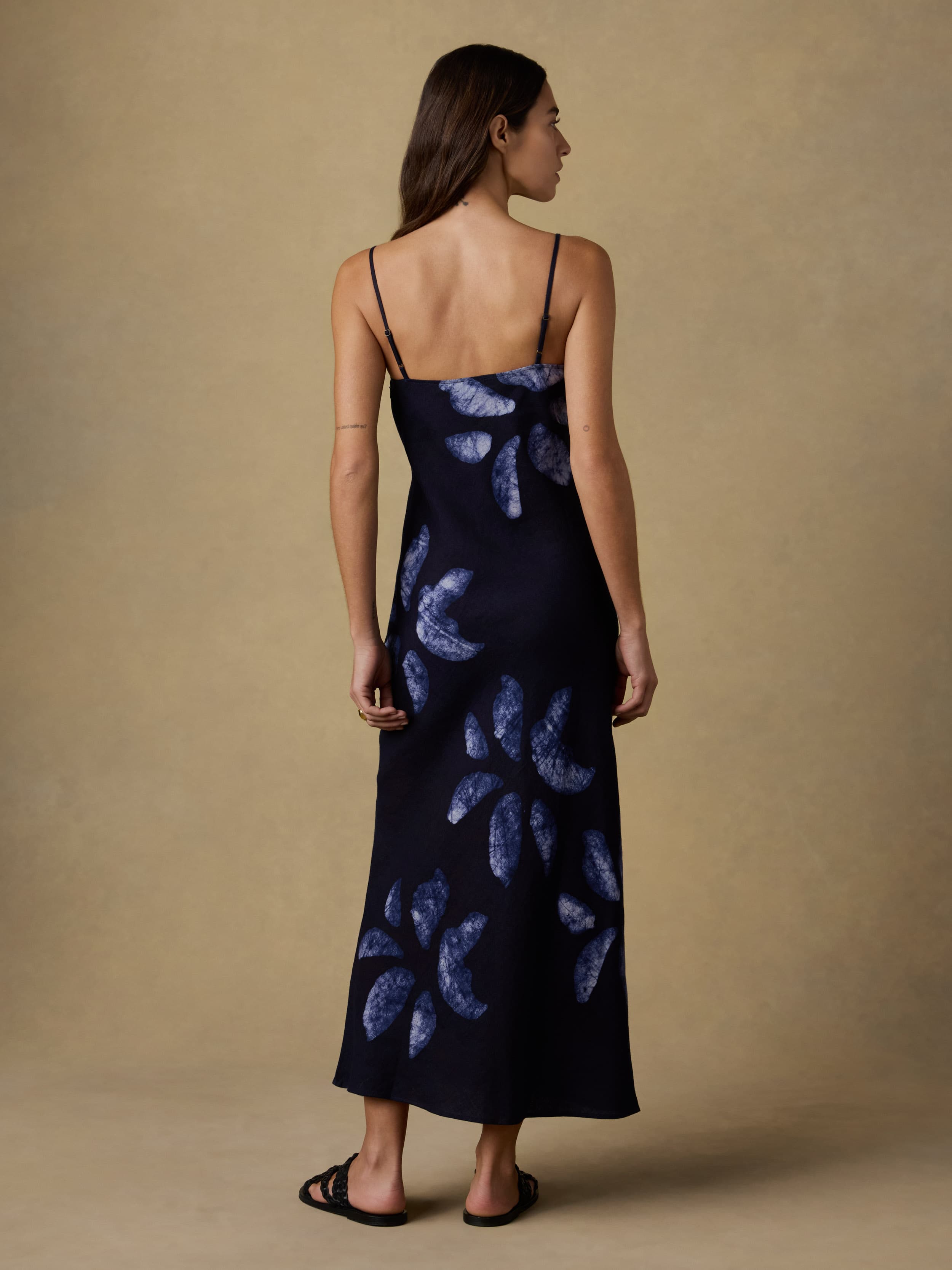 Back view of a woman wearing a dark blue dress with floral batik dye detail on a beige background