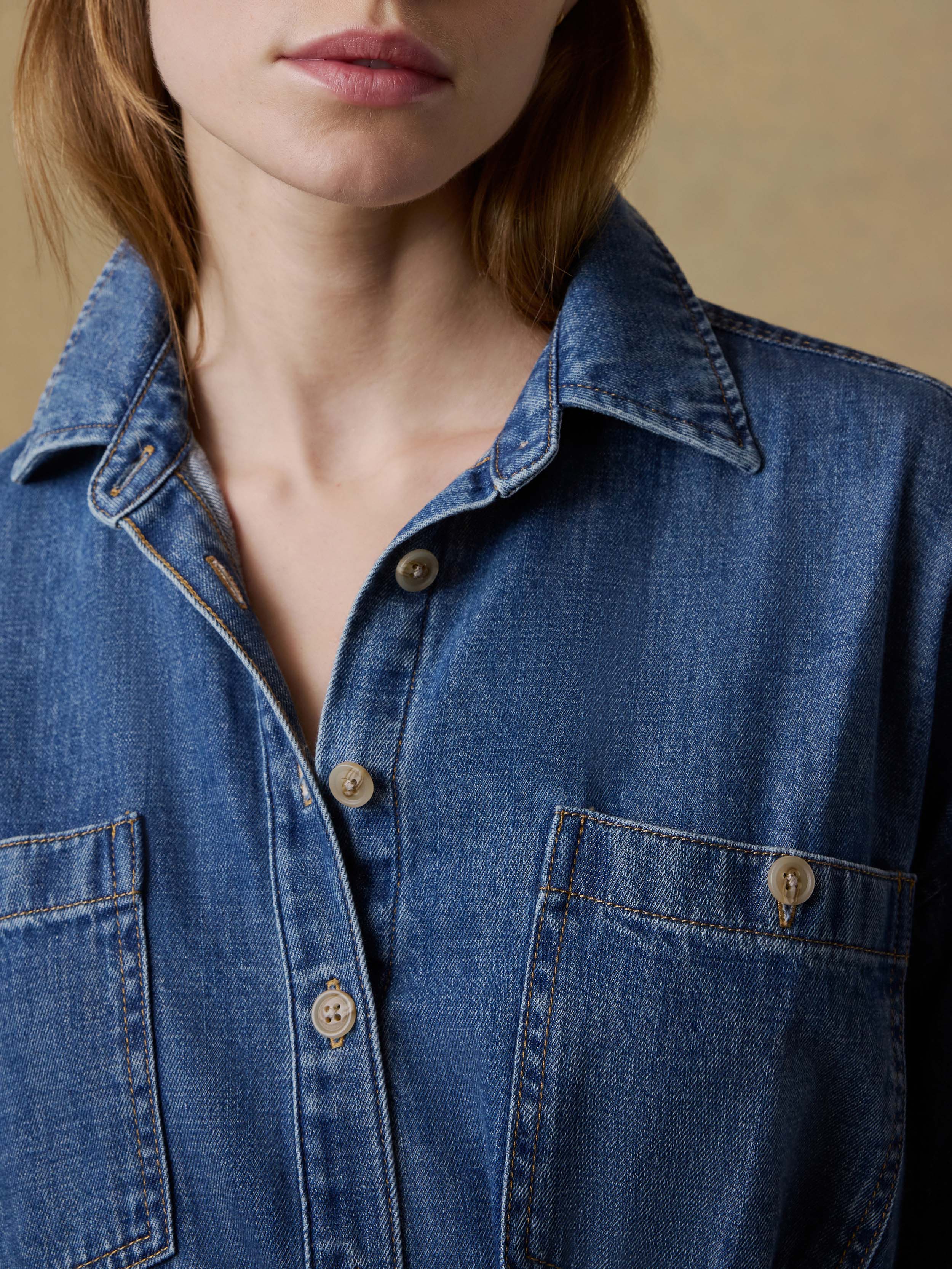 Close-up of a woman wearing a blue denim dress with a neutral background