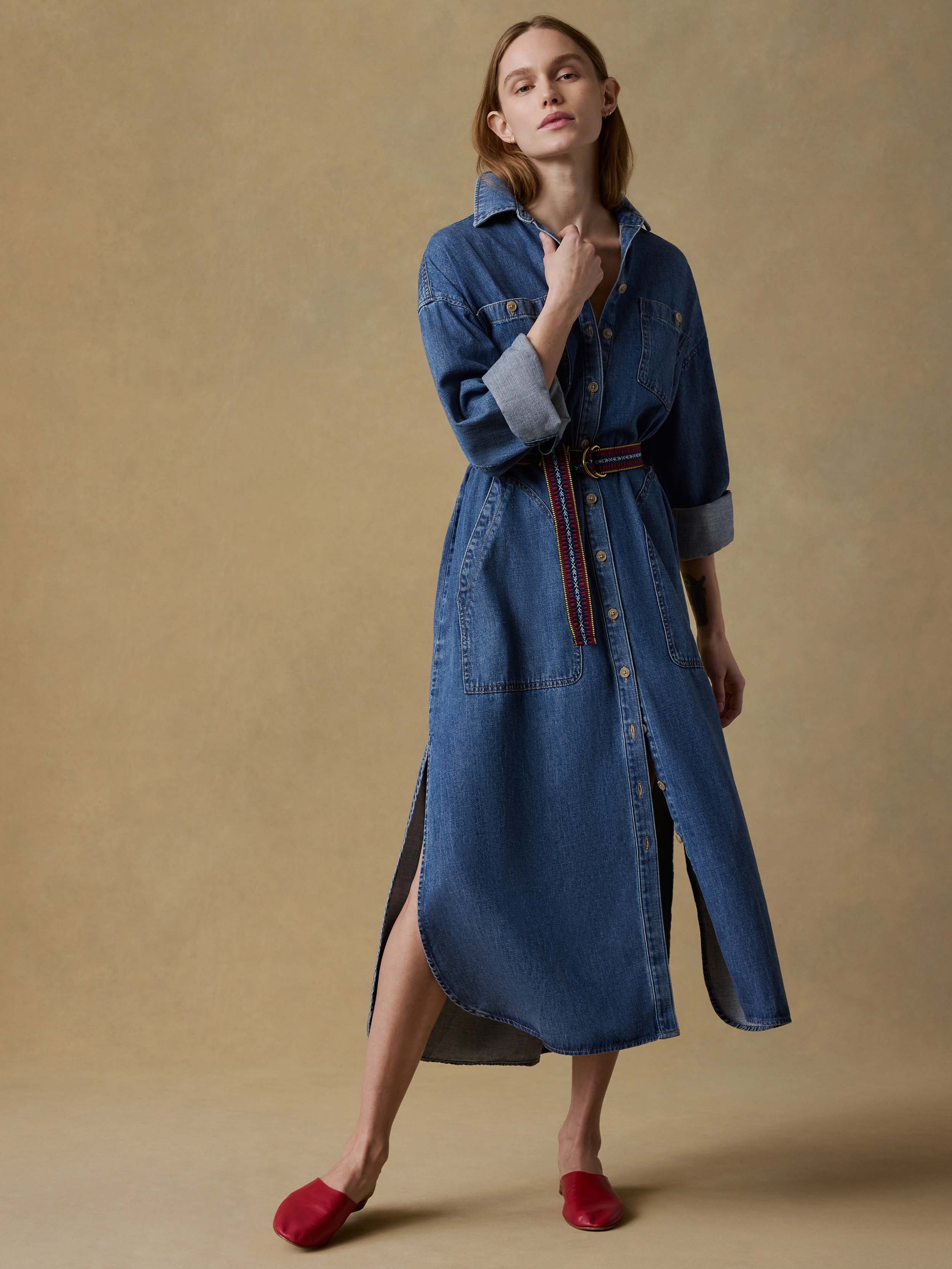 Woman wearing a long blue denim dress with a belt on a beige background