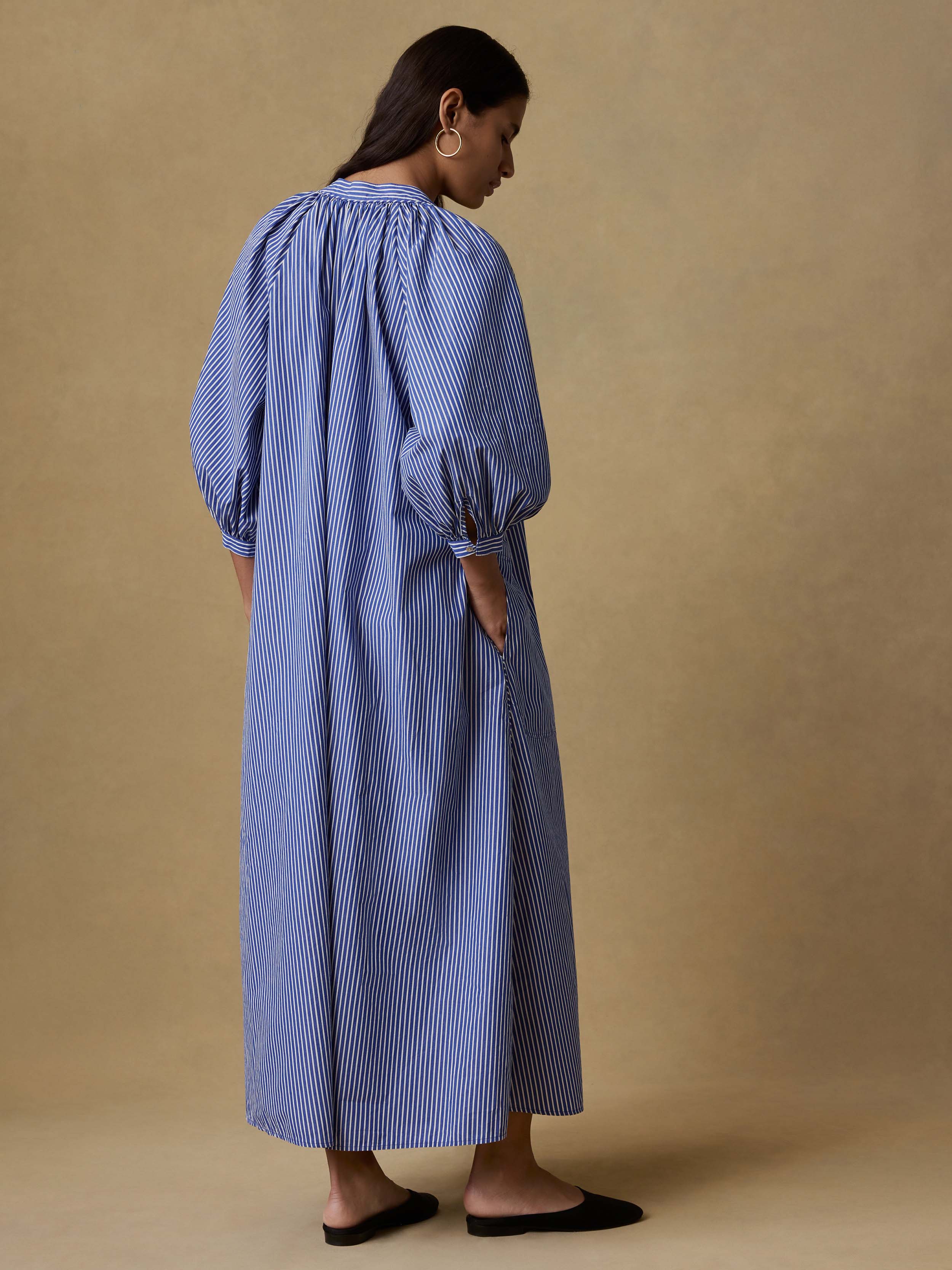 Back view of a woman wearing a blue striped dress against a beige background
