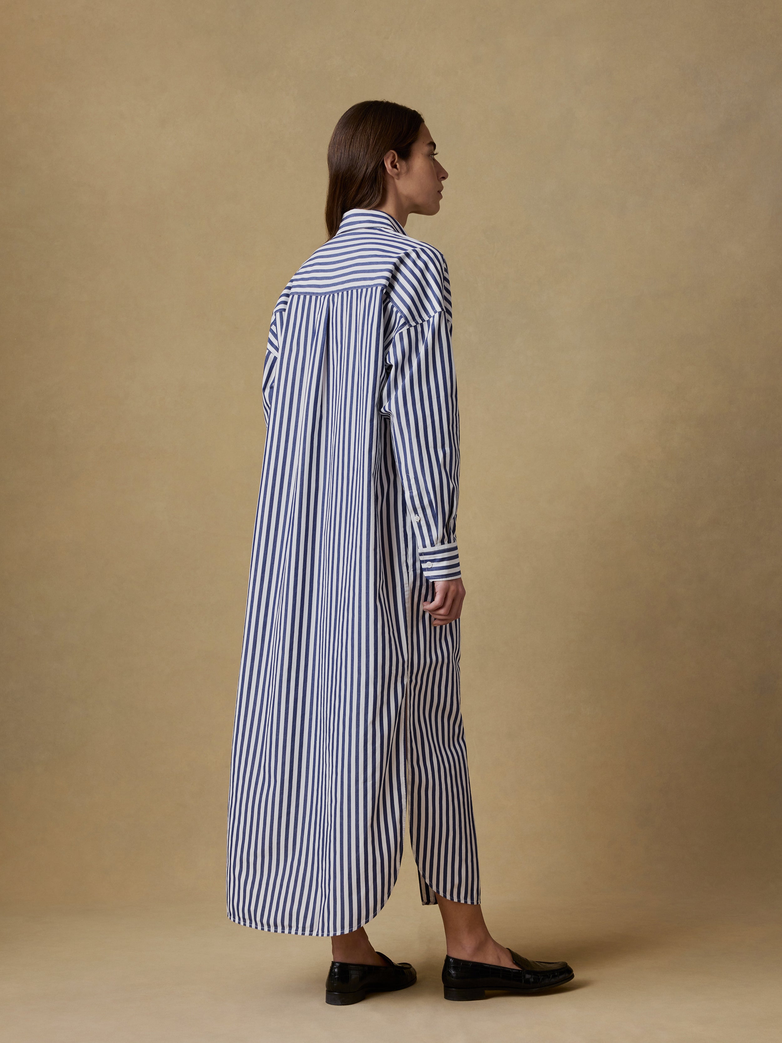 Back view of a woman wearing a long blue and white striped shirt dress against a beige background