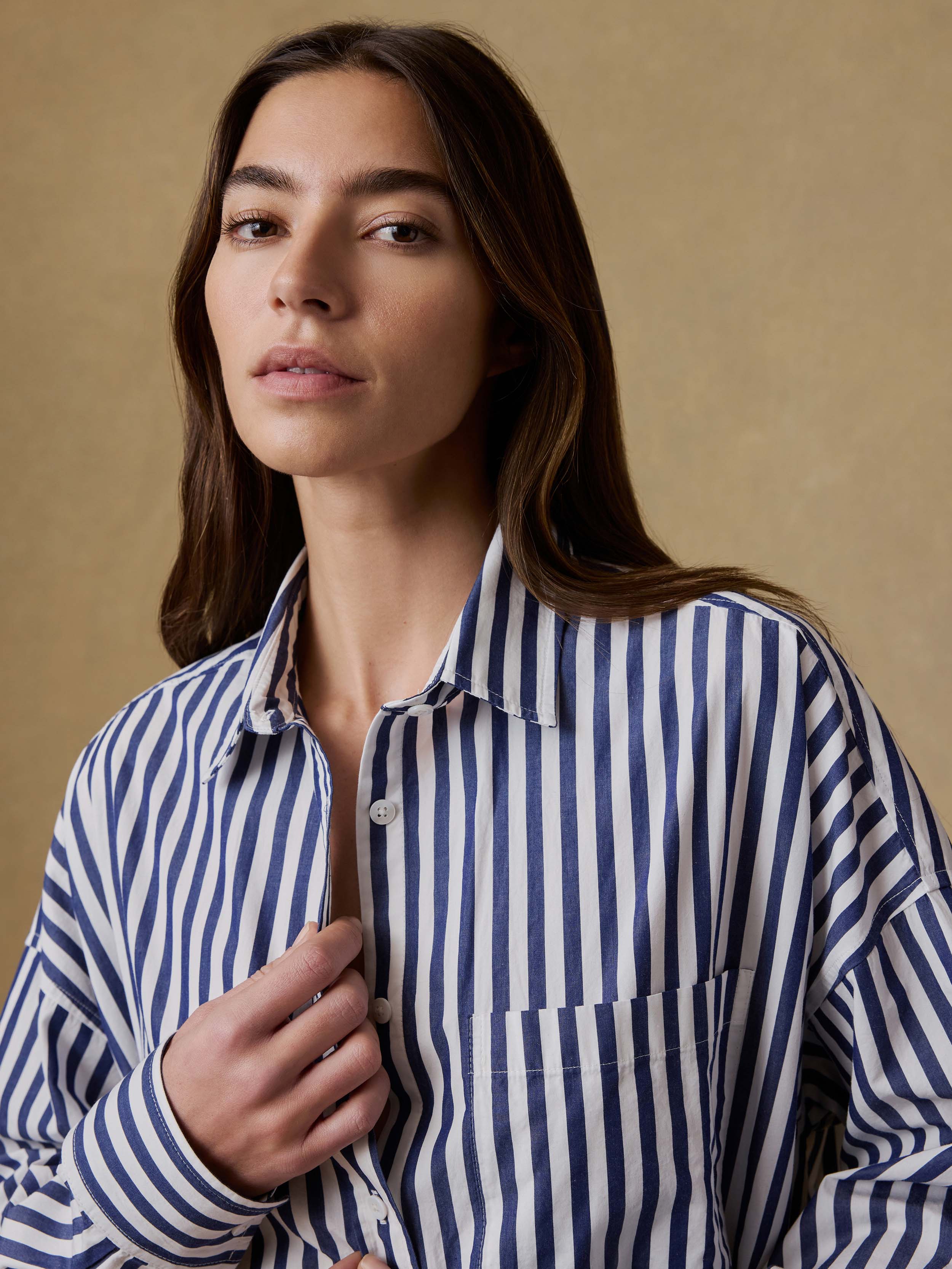 Woman wearing a blue and white striped shirt dress against a beige background