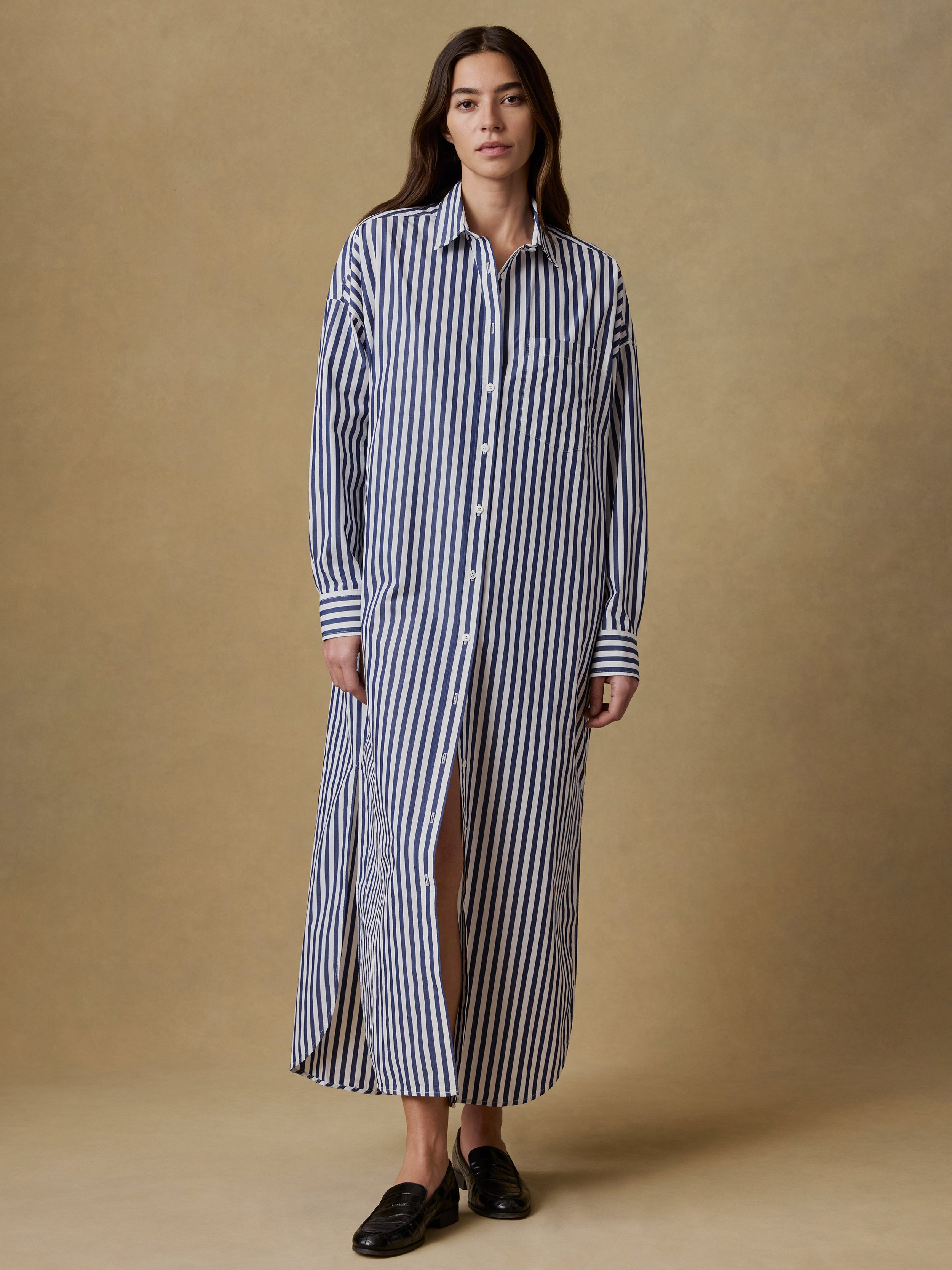 Woman wearing a long blue and white striped shirt dress against a beige background