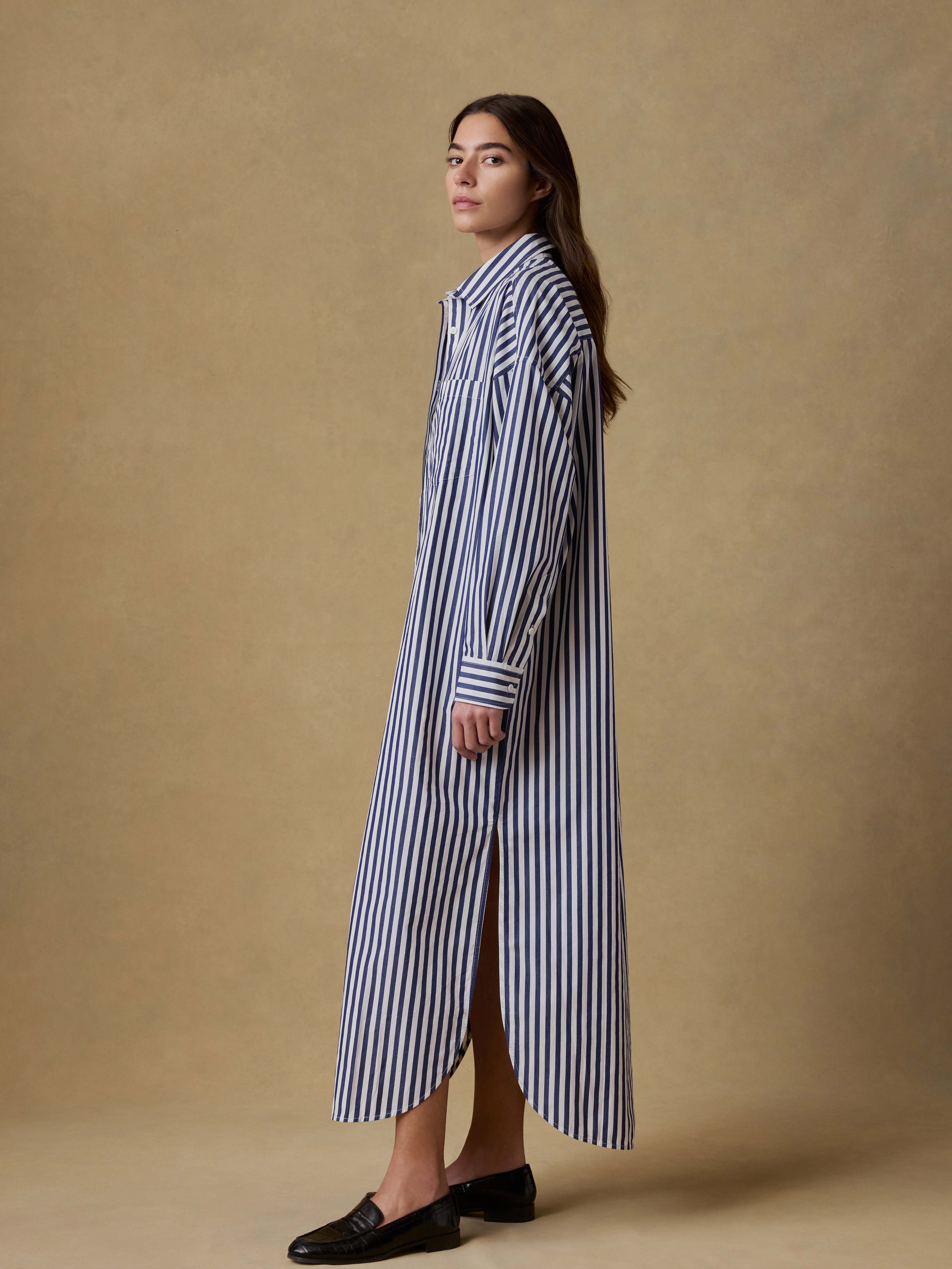 Woman wearing a long blue and white striped shirt dress against a beige background